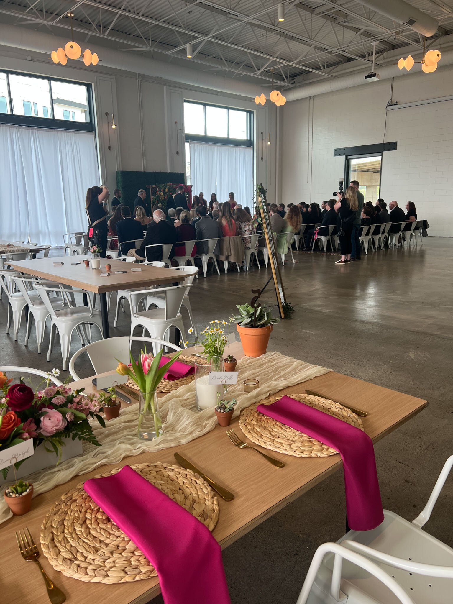 Indoor wedding ceremony with guests seated and vibrant table setup in foreground