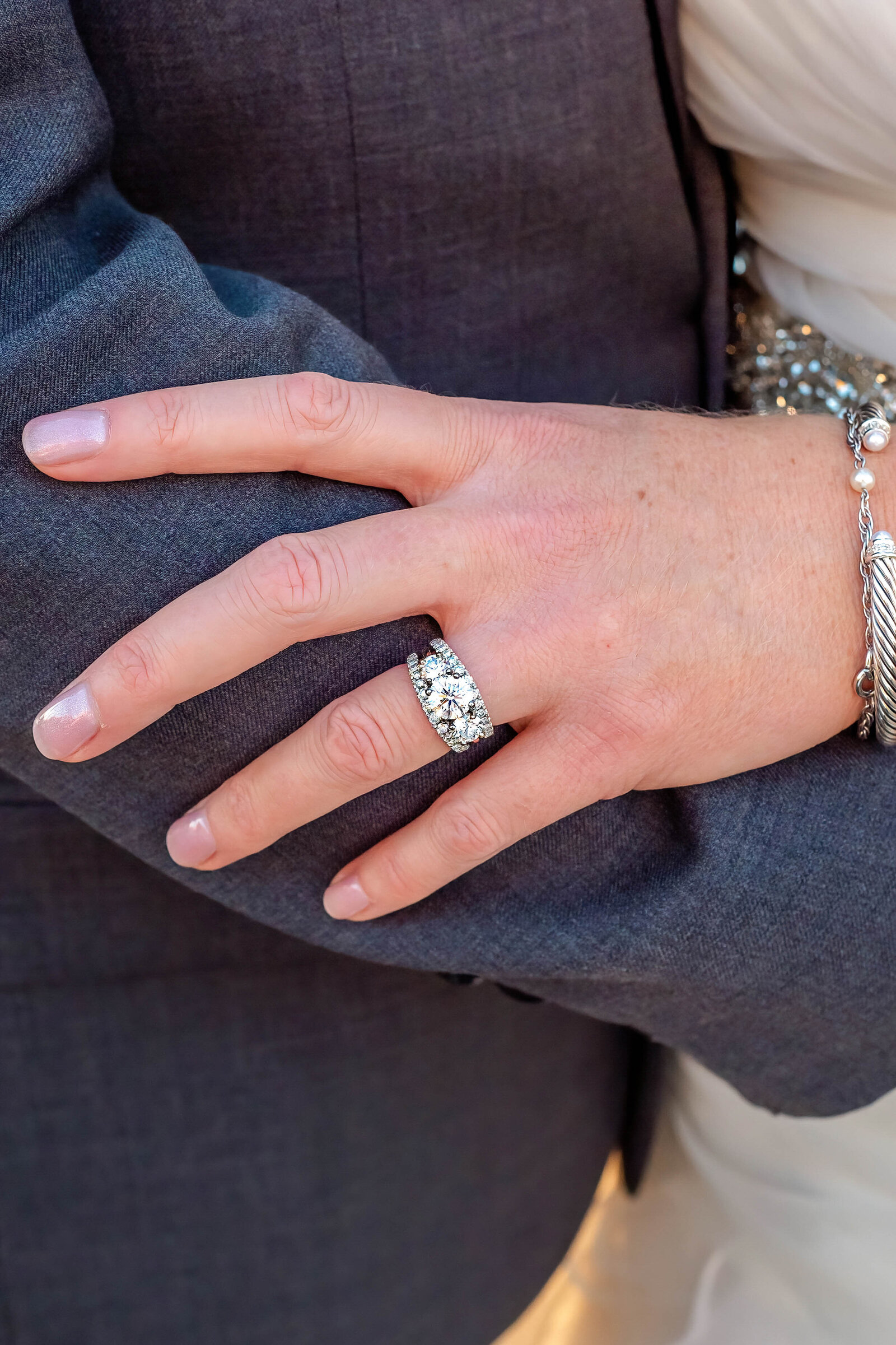 Close-up of the bride’s sparkling wedding ring and elegant bracelet resting on the groom’s suit sleeve, captured during a Wilmington, NC wedding, showcasing timeless and refined wedding details.