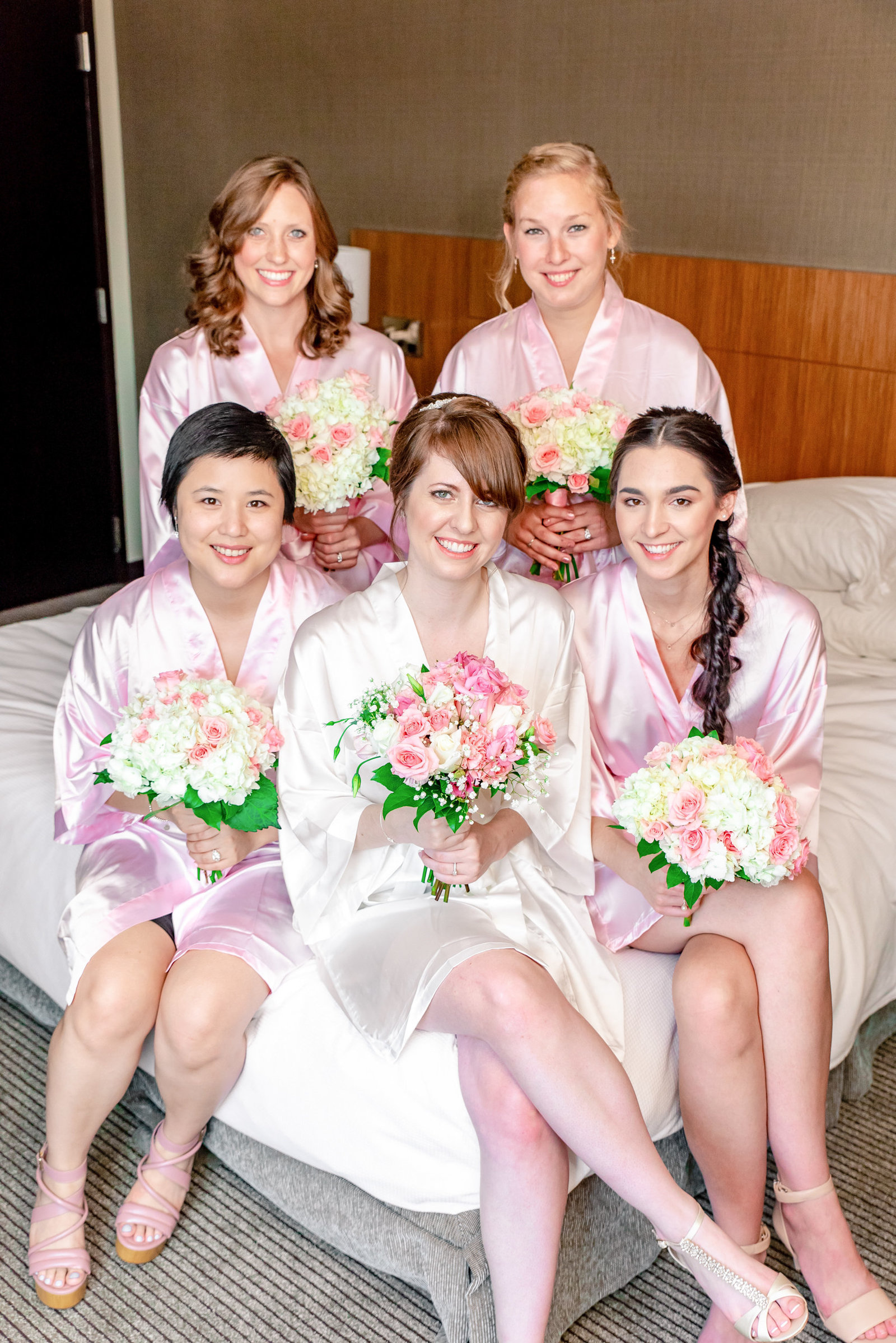 bridesmaids and bride pose on a bed for a photo