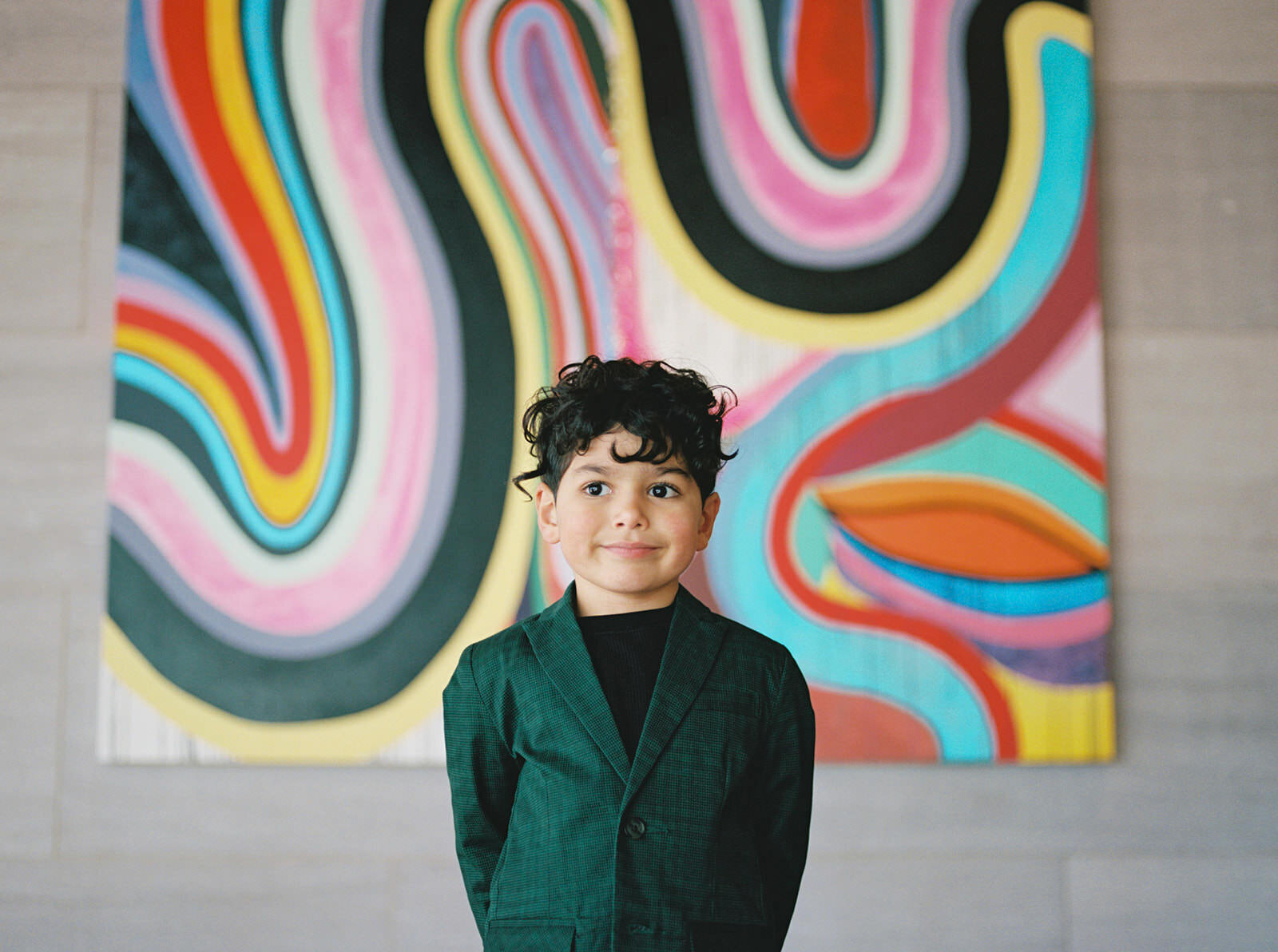 A vibrant portrait of a young boy standing confidently in front of colorful abstract artwork in a gallery, exuding charm and personality.