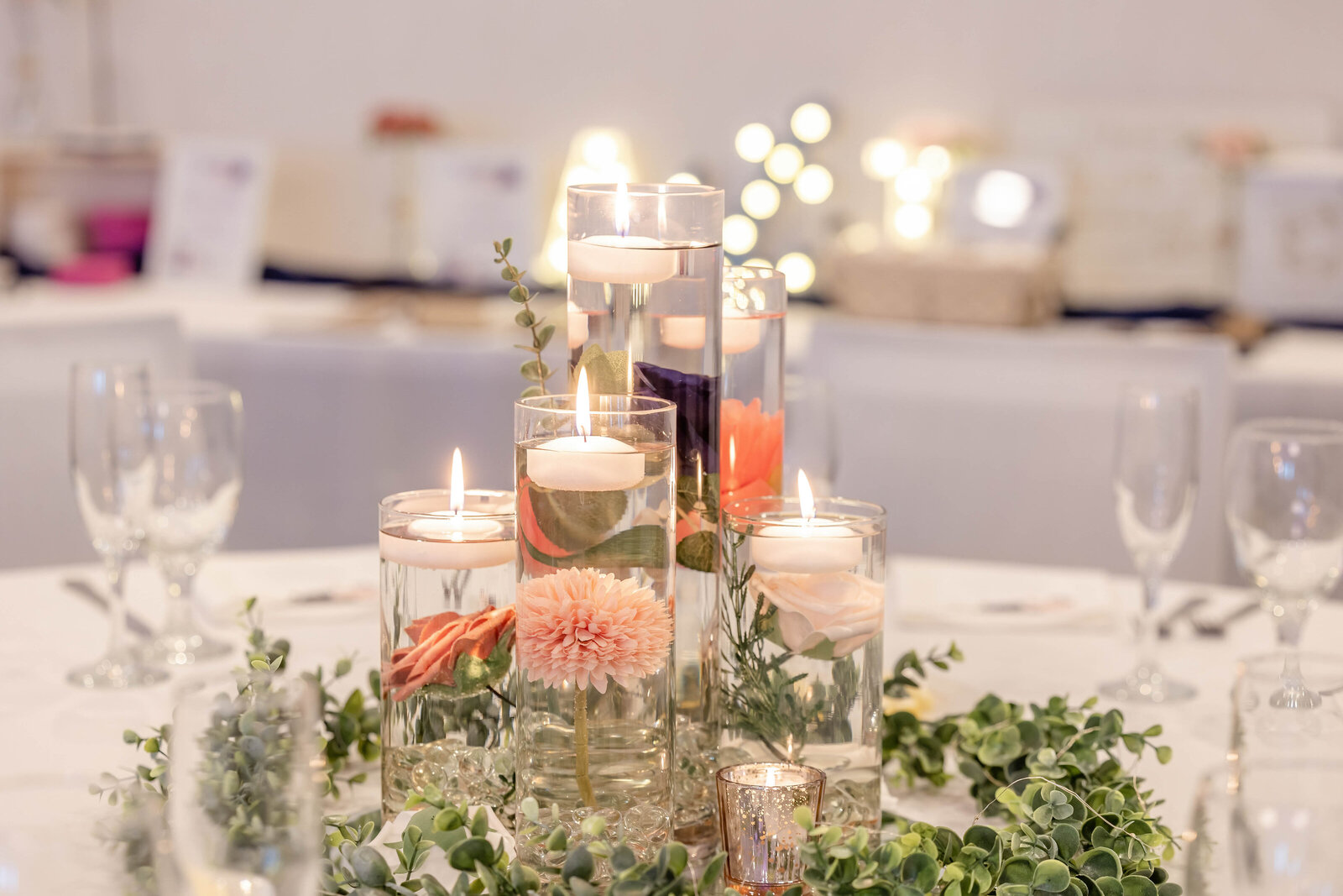 A stunning wedding reception centerpiece featuring floating candles, vibrant coral and pink flowers, and lush greenery, captured at a Carolina Beach, NC wedding venue with a rustic yet elegant ambiance.