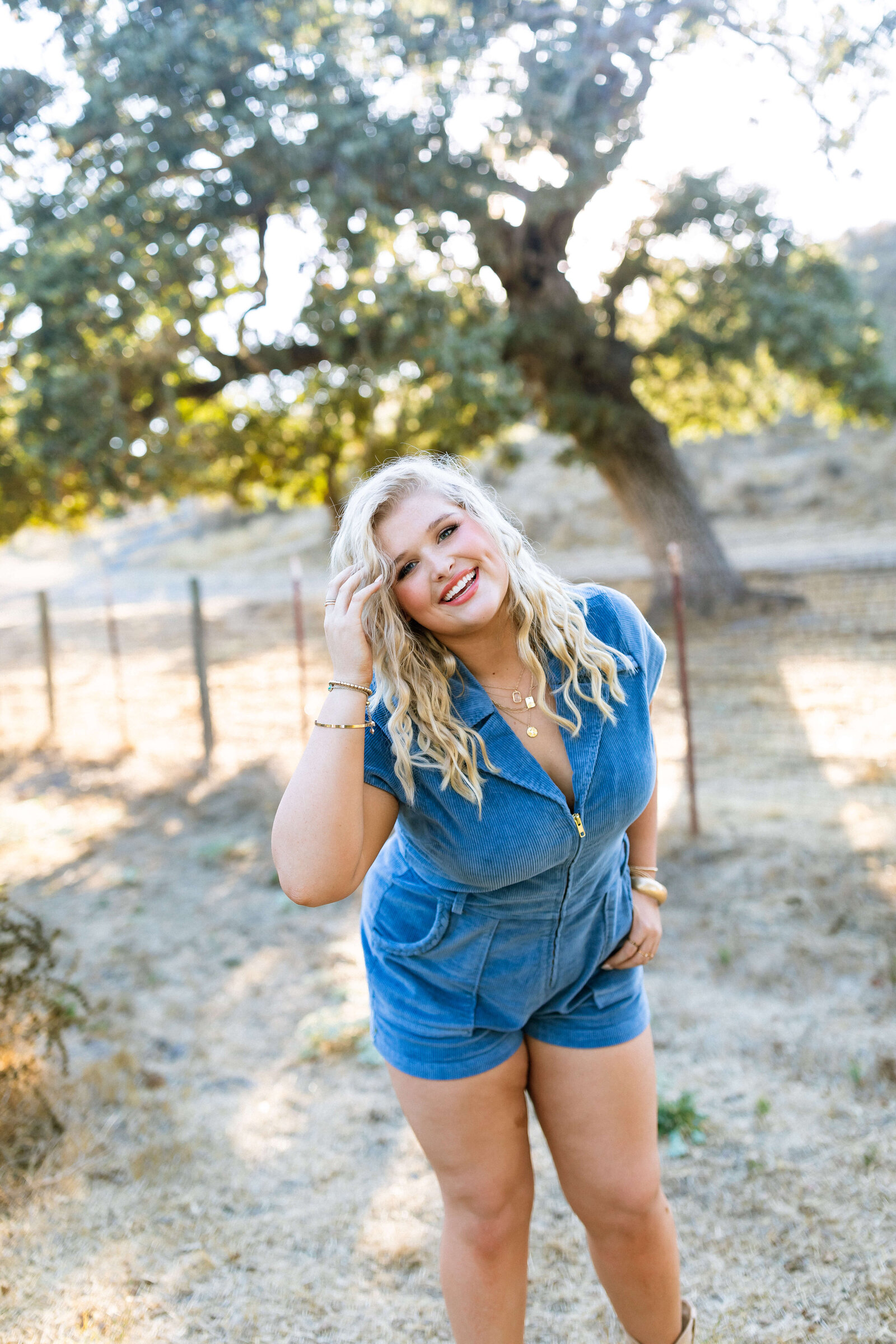 blonde girl wearing blue jean romper smiling and posing in a ranch