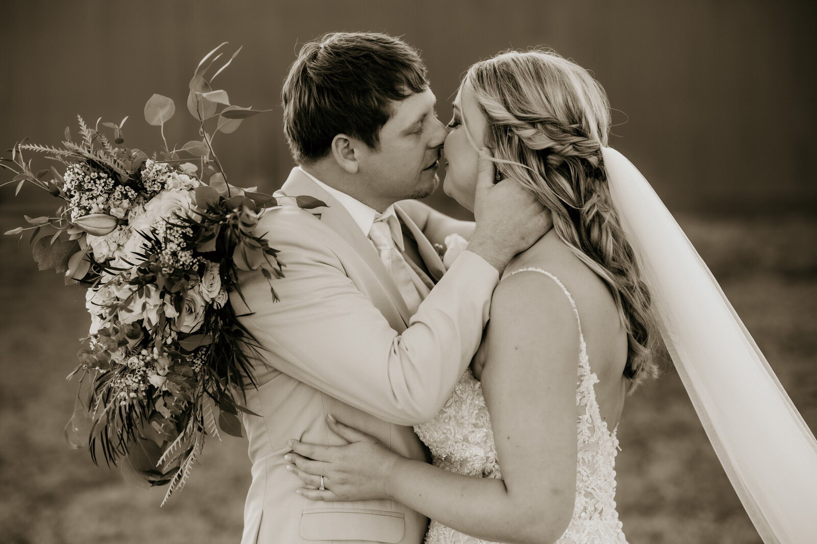 Best Little Rock wedding photographer photographs bride and groom kissing as they embrace in front of an old barn