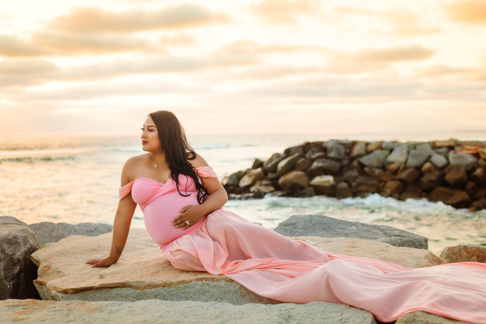 Maternity Photographer, a pregnant woman wears a gown and reclines on beach rocks