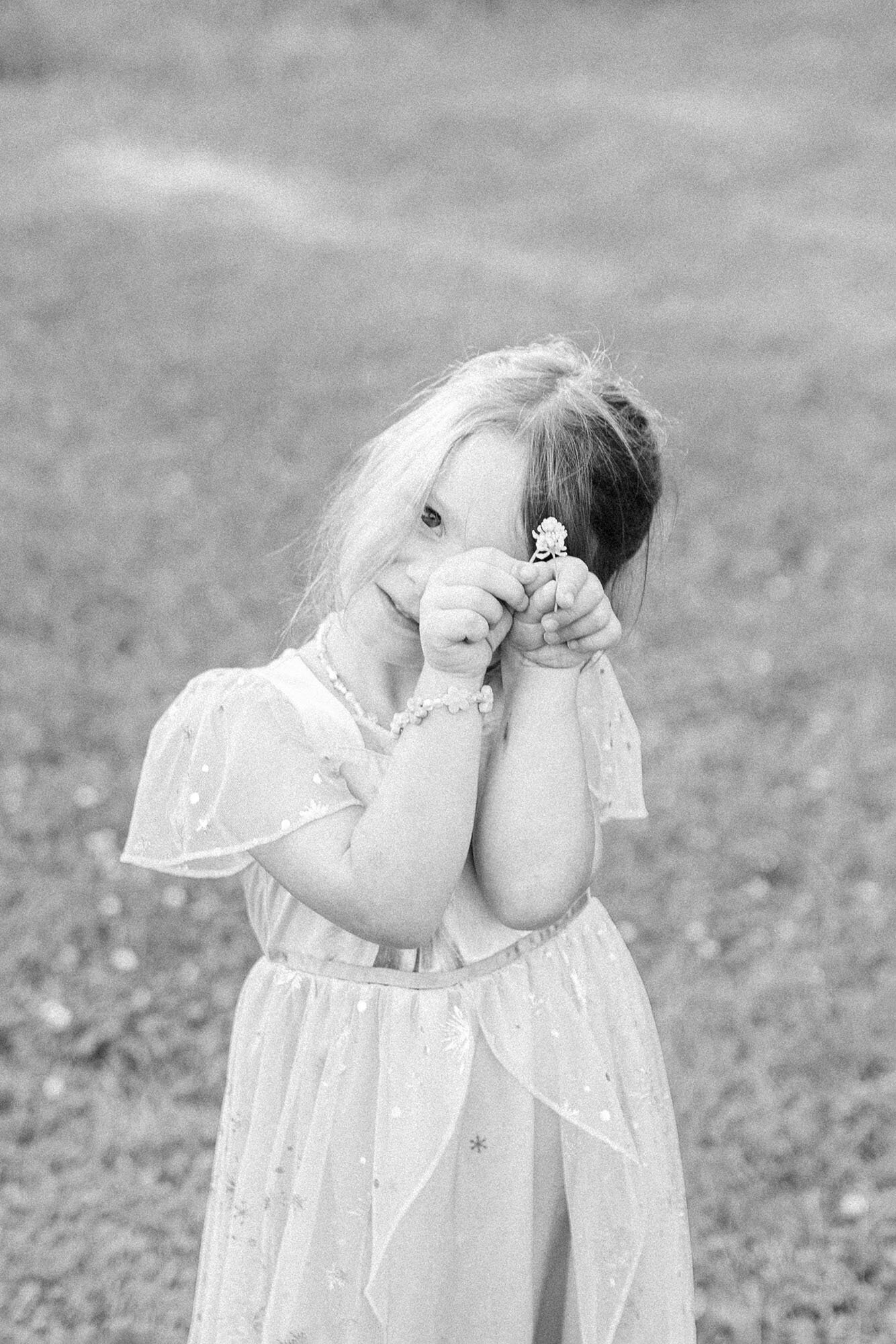 A little girl holding a flower over her eye during her sunset photo session