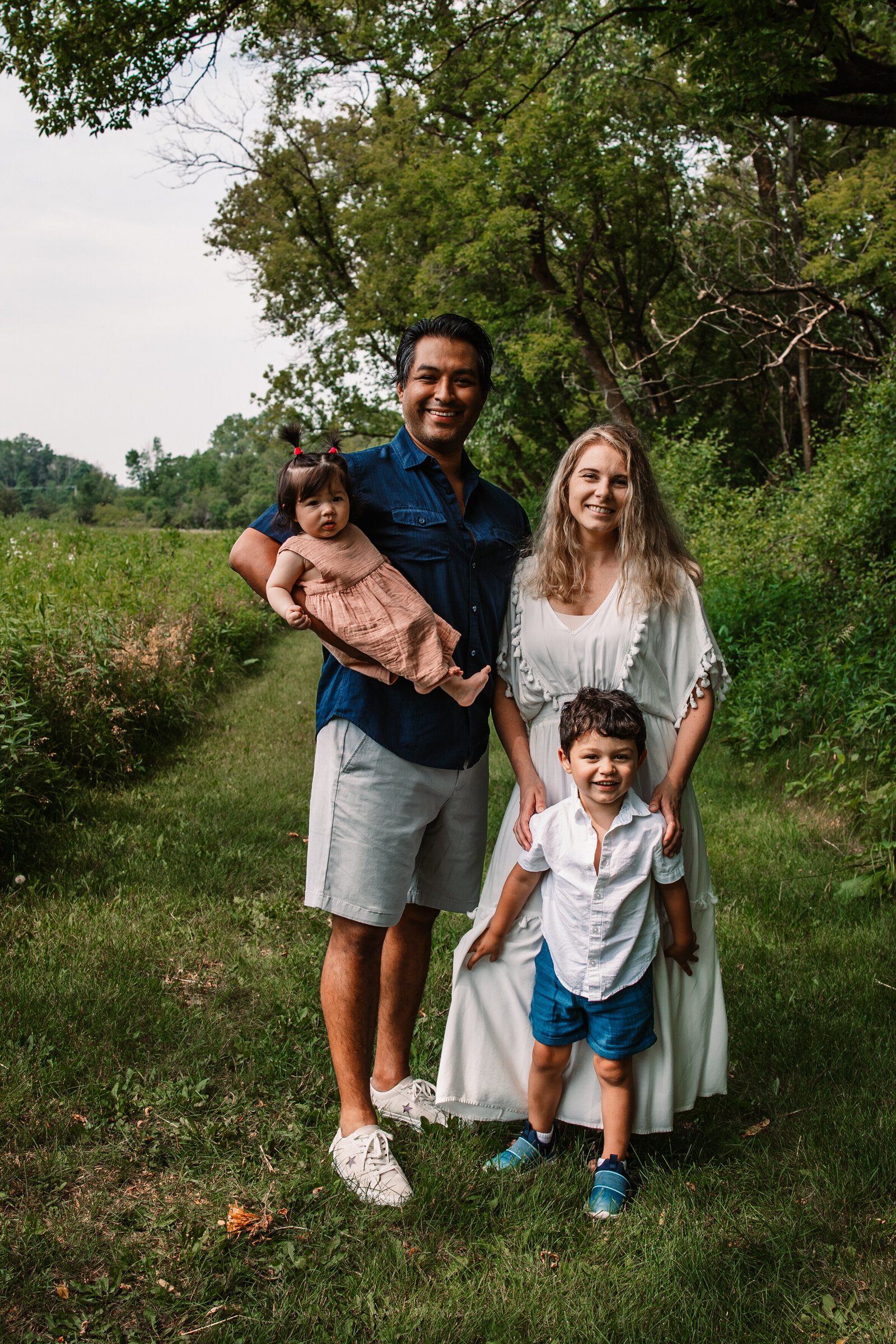 A family of 4 with 2 toddlers in blue and white explore a park trail together