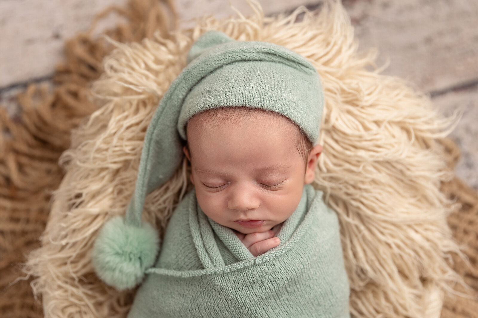 baby in green hat and swaddle on faux fur throw
