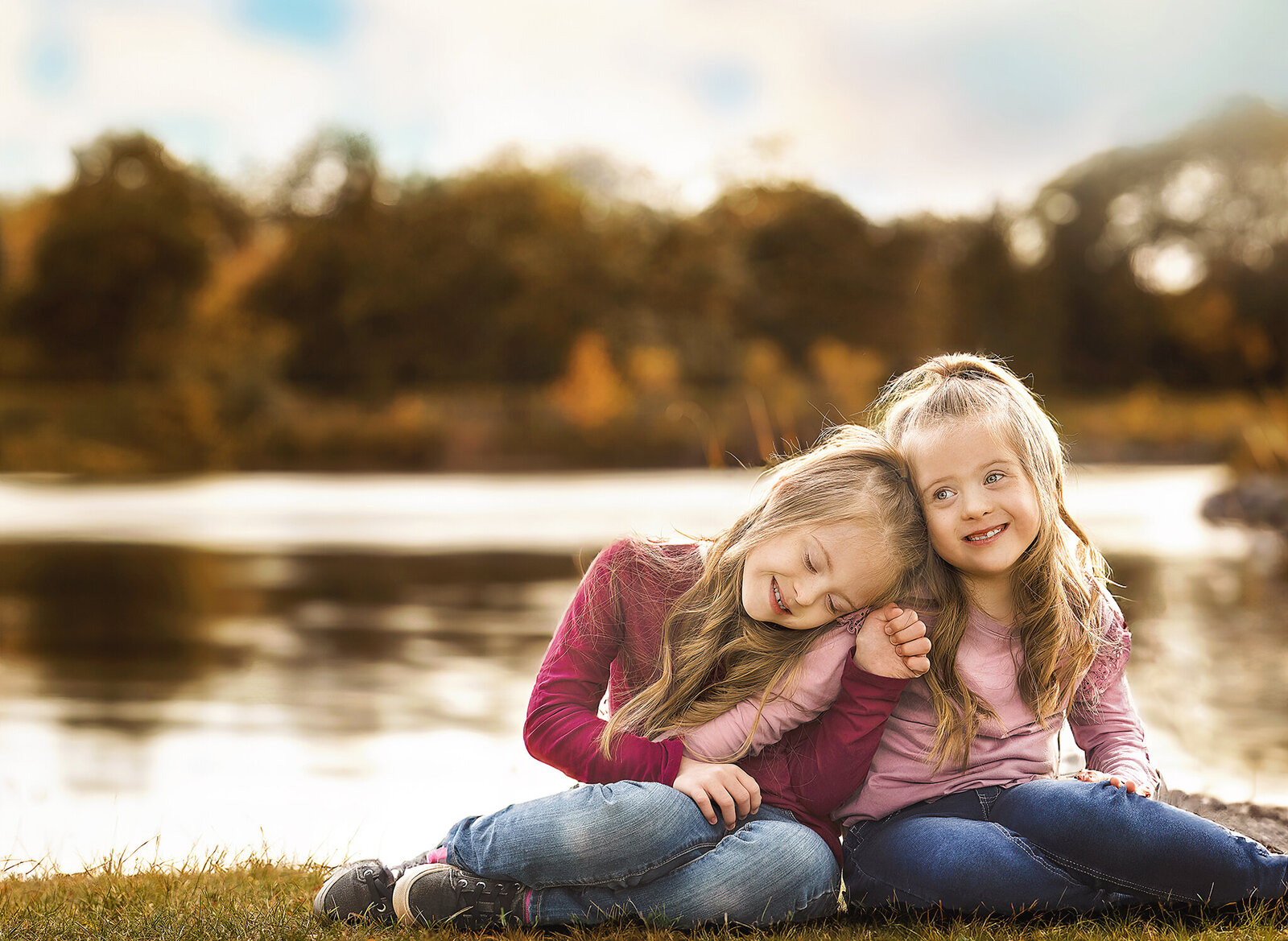 Sisters sitting in front of lake and fall trees
