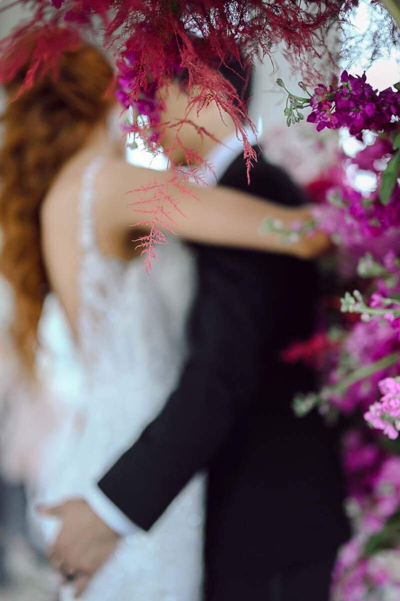 artistically blurred photo of bride and groom embracing each other with floral details in the foreground