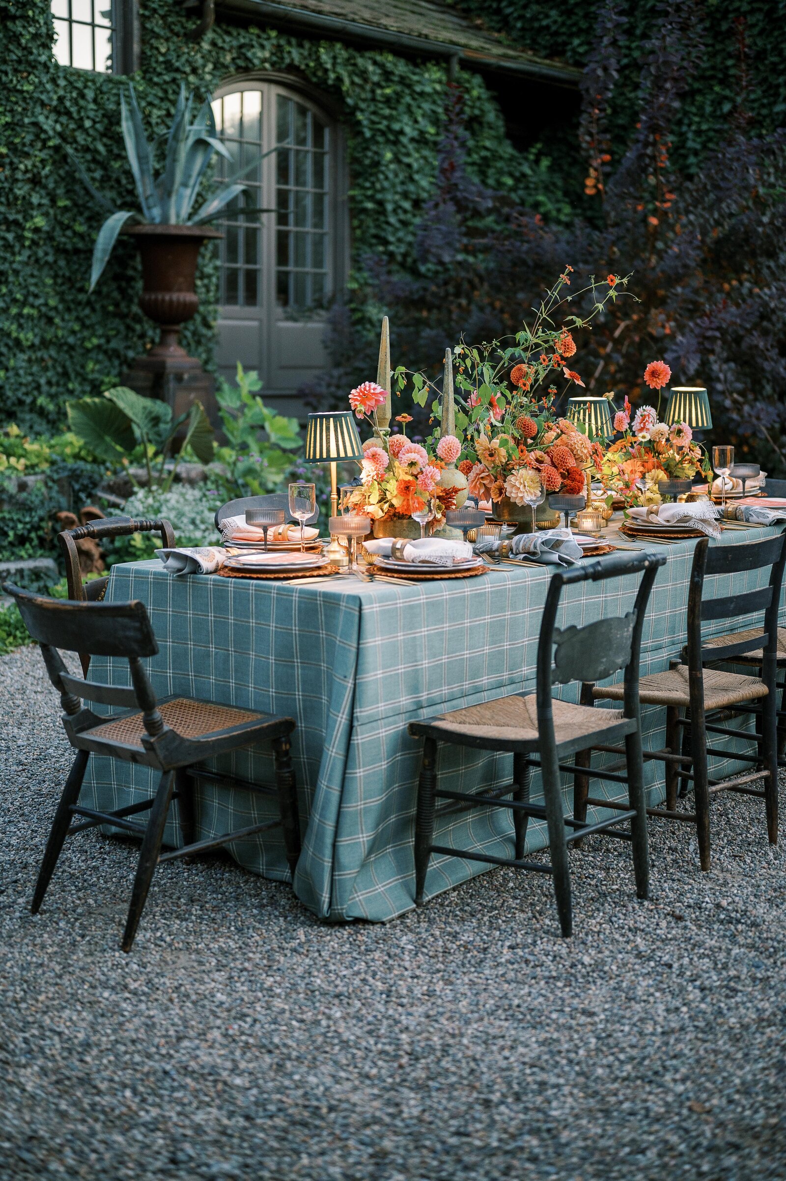 Romantic outdoor wedding reception with a rustic wooden table, plaid tablecloth, and lush floral centerpieces in warm hues.