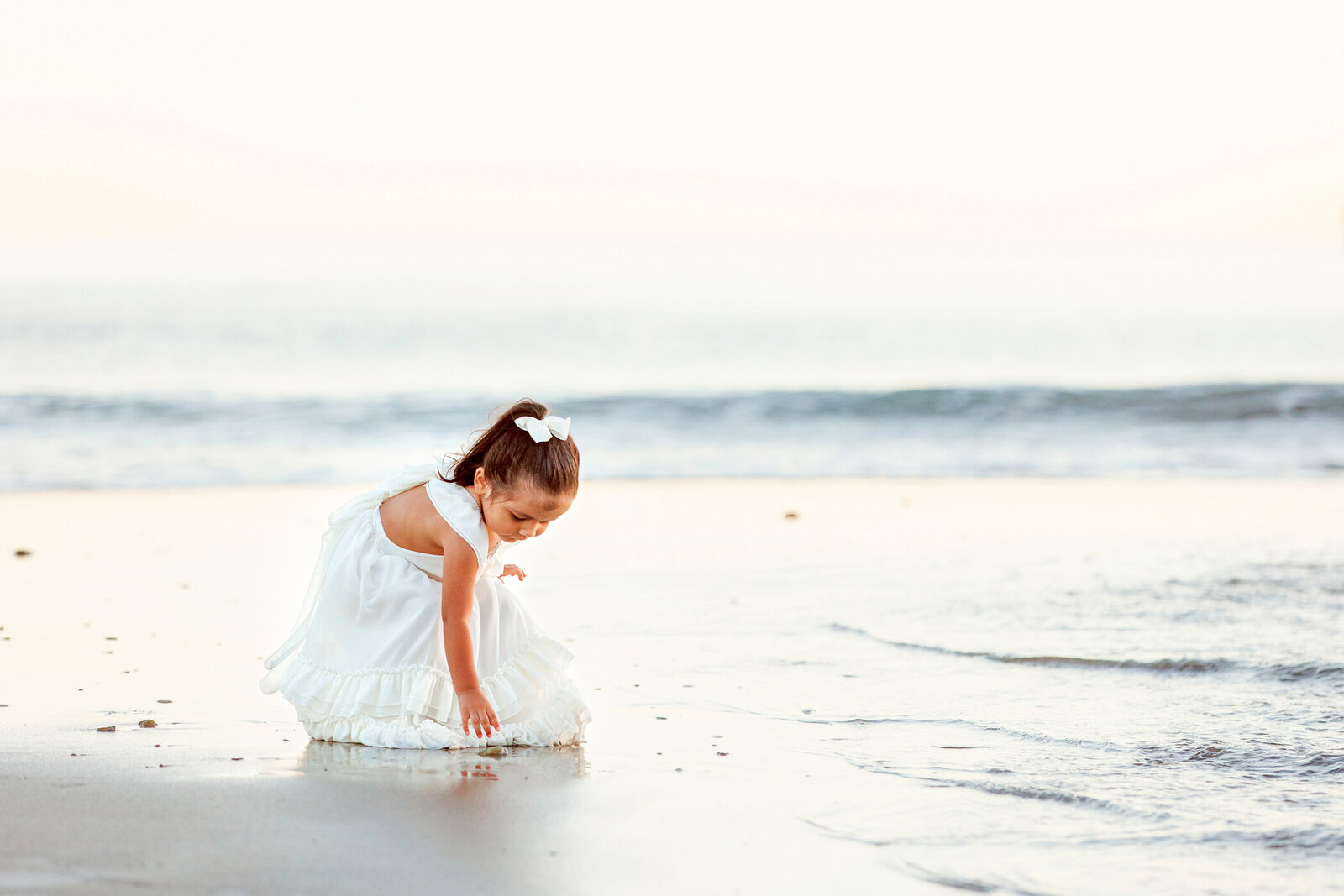Little girl in  a flowy white dress picking seashells in the sand. Ethereal portrait. San Luis Obispo, Pismo Beach, Avila Beach, One Good Shot Photography