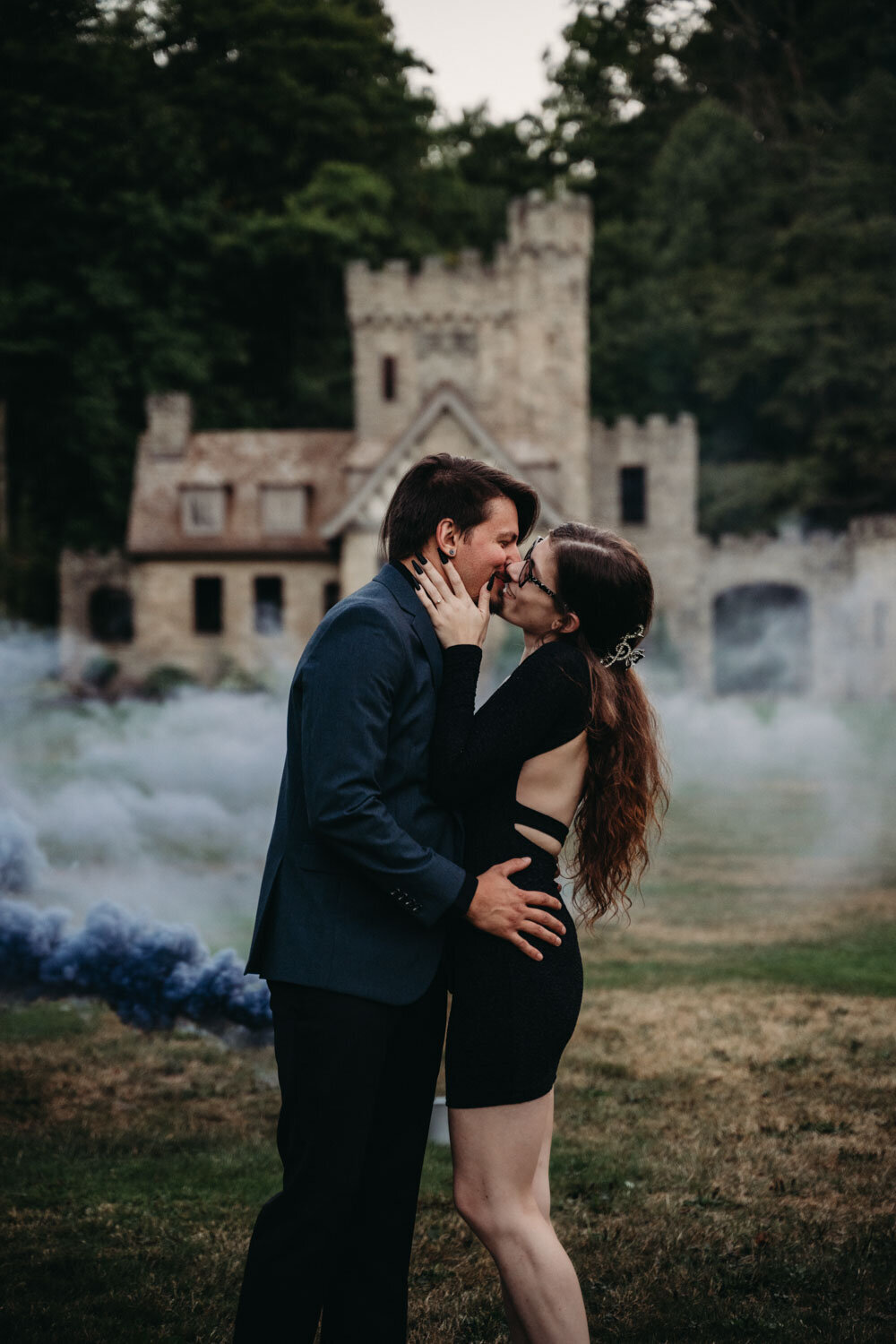 Couple dressed alterntively kisses with black smoke bomb behind them