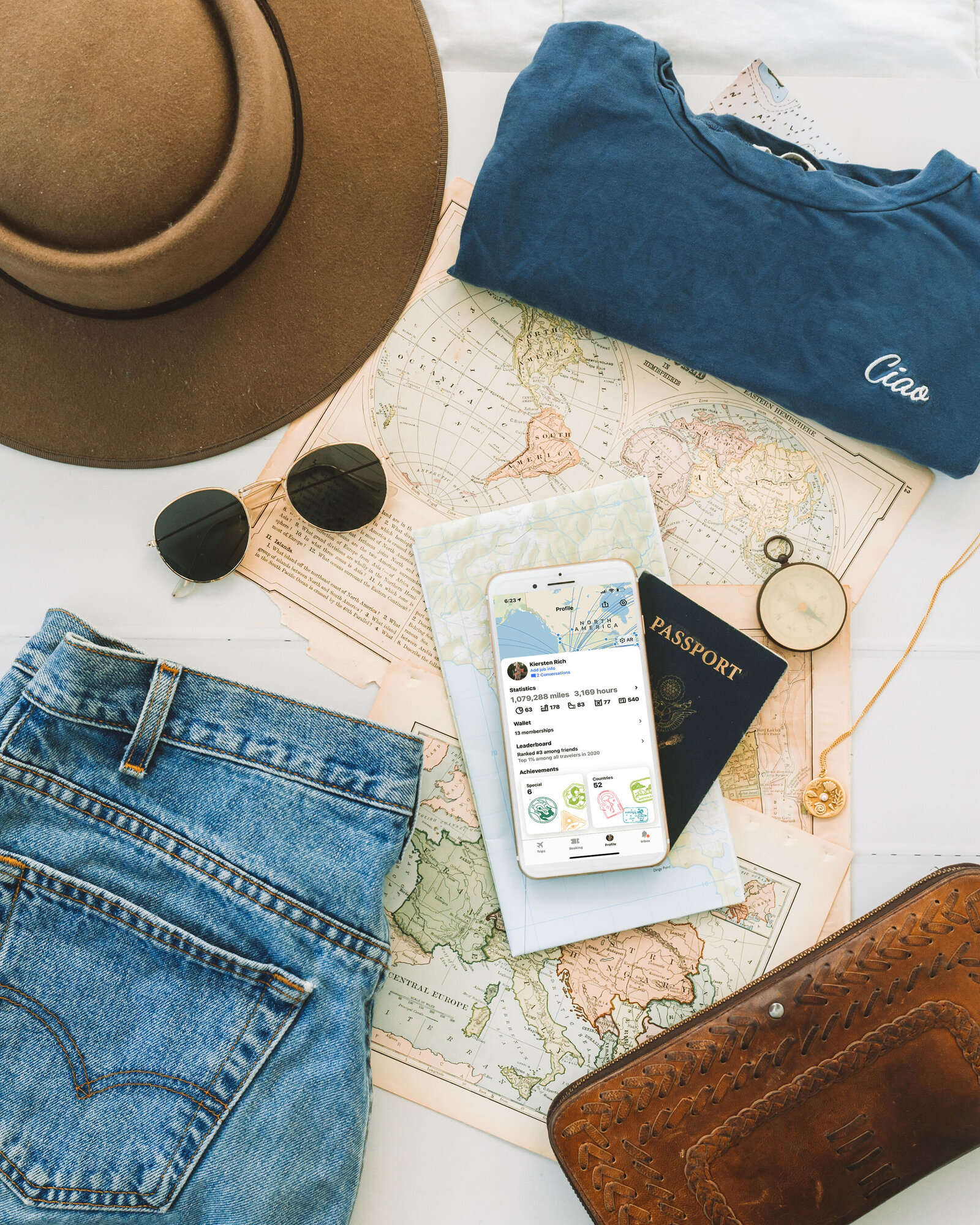 Styled flat lay of a mobile travel application by product photographer Chelsea Loren. Rustic hat, Levi jean shorts, wallet, passport, compass, sunglasses