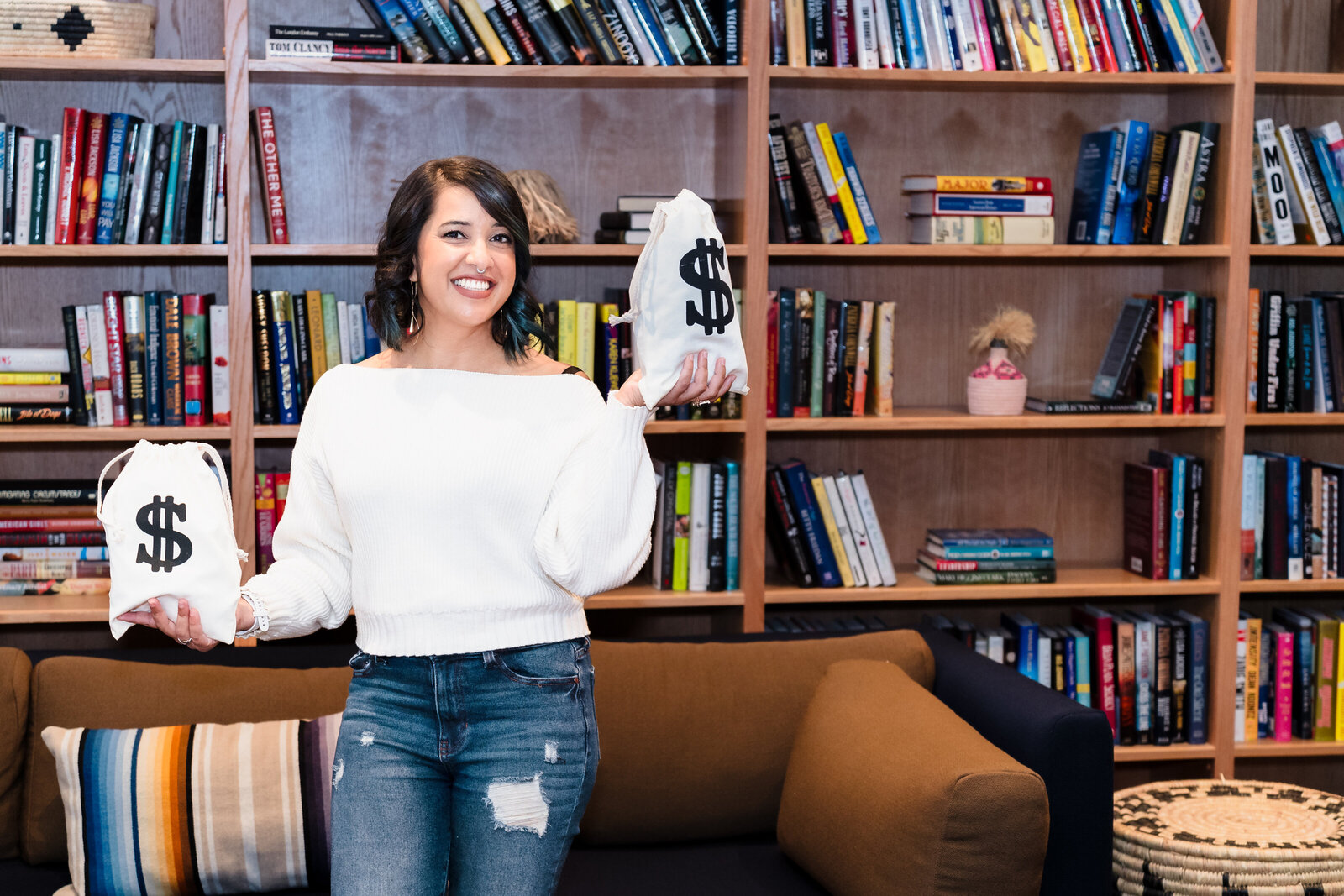 Business Coach holds two bags with money sign, background is a library