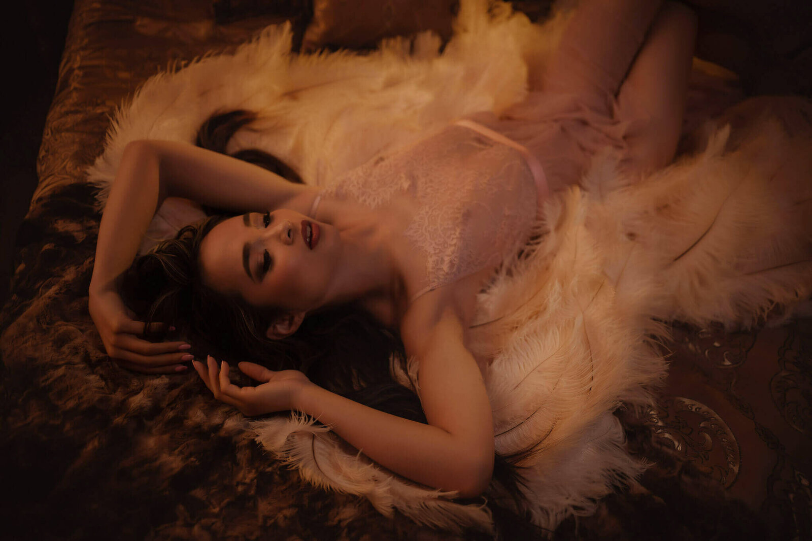 Woman in a pink nighty wearing angel wings lying on a bed in a  boudoir studio near Fort Worth