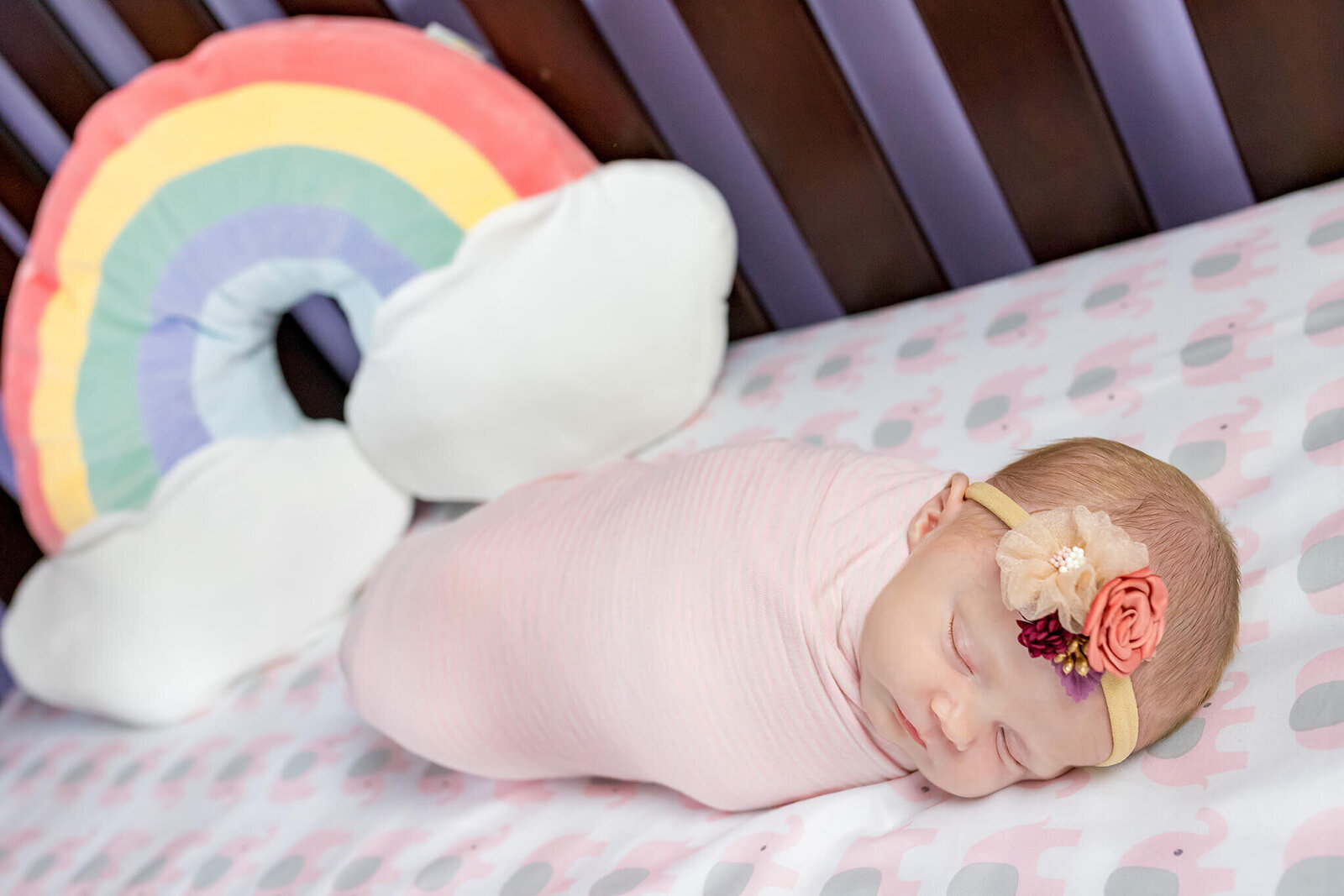 A newborn girl in her crib with a rainbow pillow in Manassas.