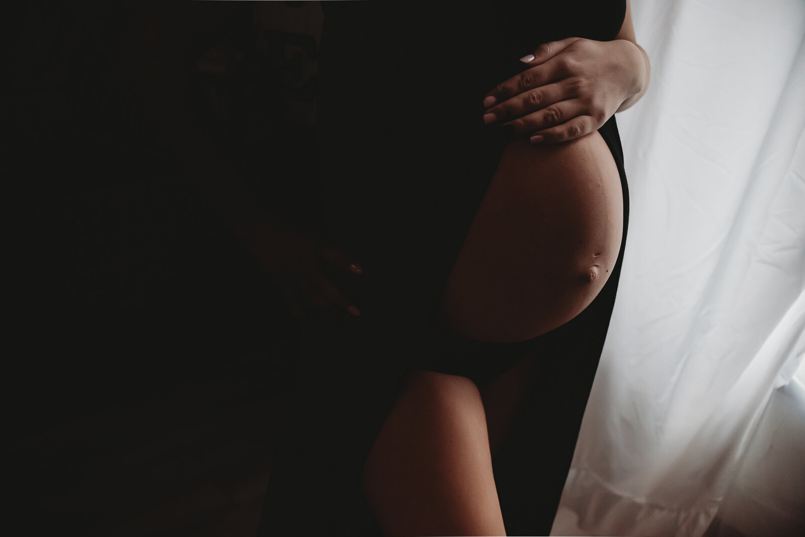 A momma embraces her baby bump with a moody feel during her maternity session in the studio of Nikii Pix Photography