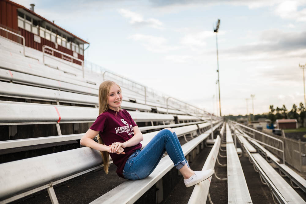 senior in henderson county colonols shirt sitting in football stadium at henderson county high school by senior photographer in henderson ky klem photography