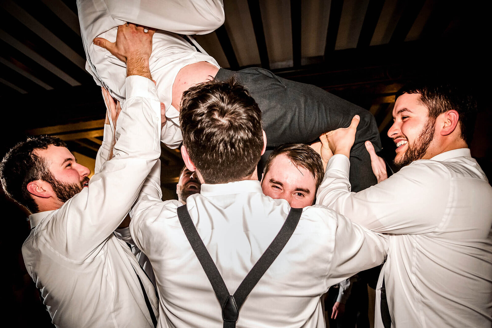 Groomsmen lifting groom at wedding reception