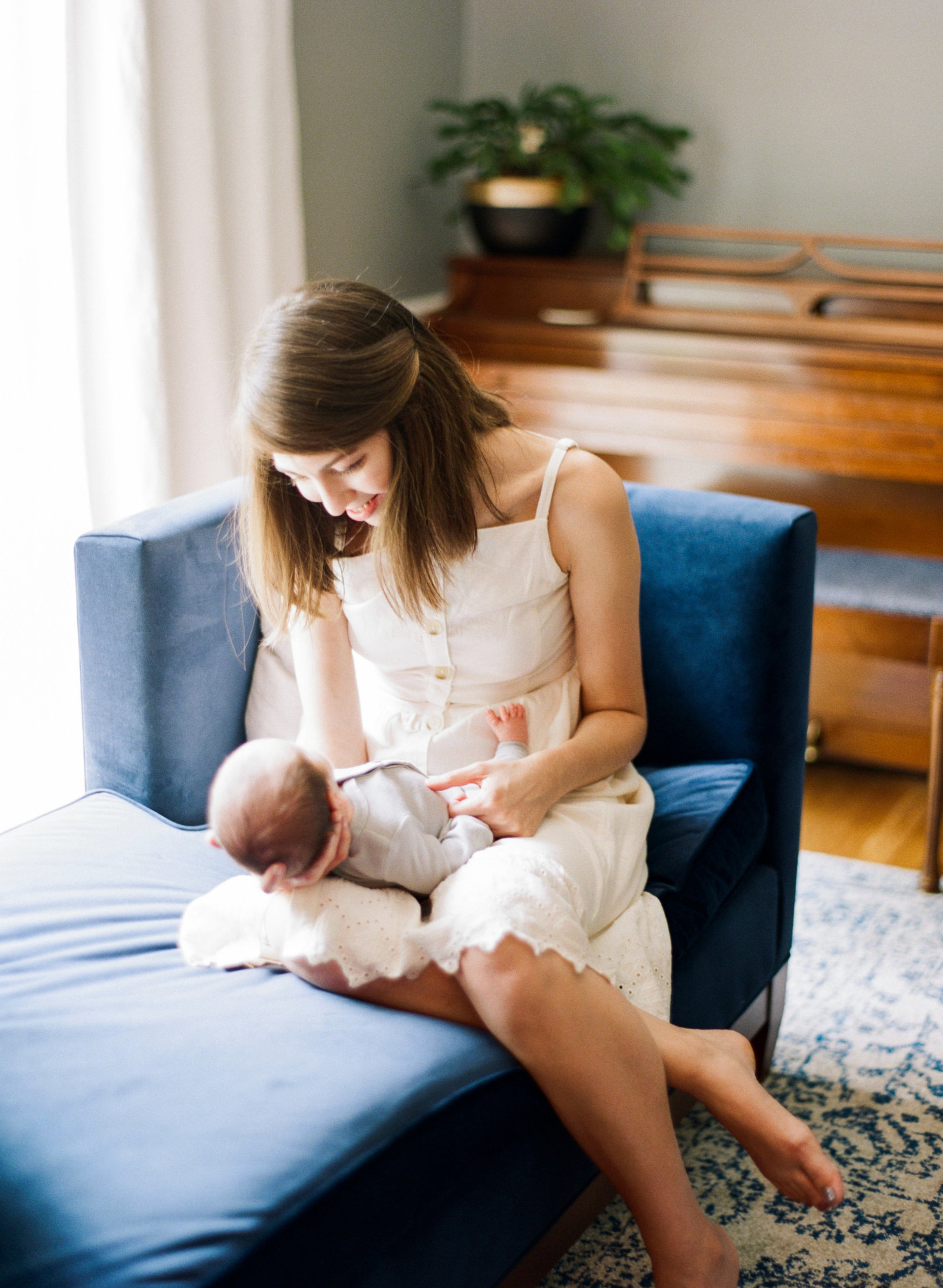 Mom snuggling her newborn baby boy on a blue couch while smiling at him during her Raleigh newborn session. Photographed by Raleigh newborn photographer A.J. Dunlap Photography