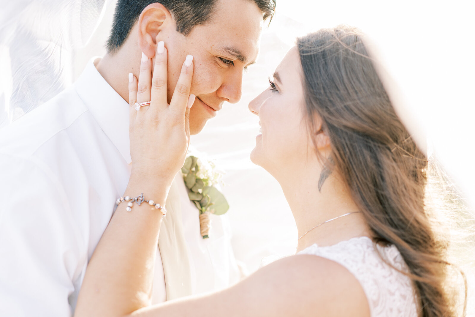 Portrait of bride and groom in a white wedding gown and white suit sharing an embrace.