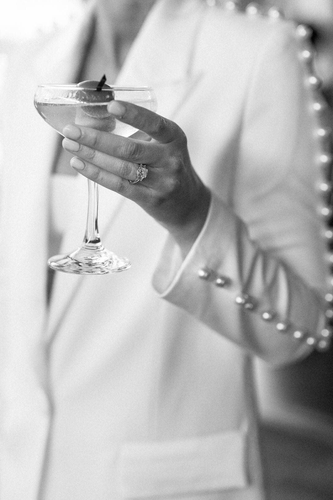 Black and White of Bride Holding a Martini wearing a white coat with pearls down the sleeve