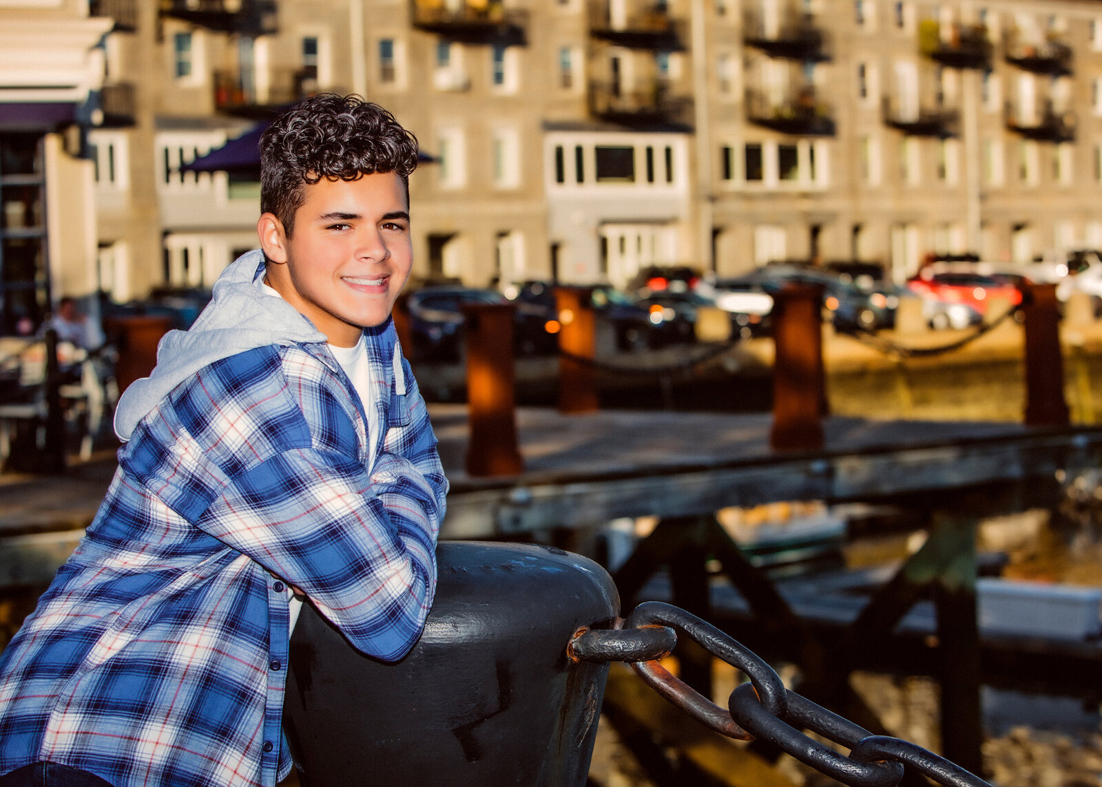  High school senior boy leaning against a metal fence overlooking Boston Harbor while posing for a Boston Photographer