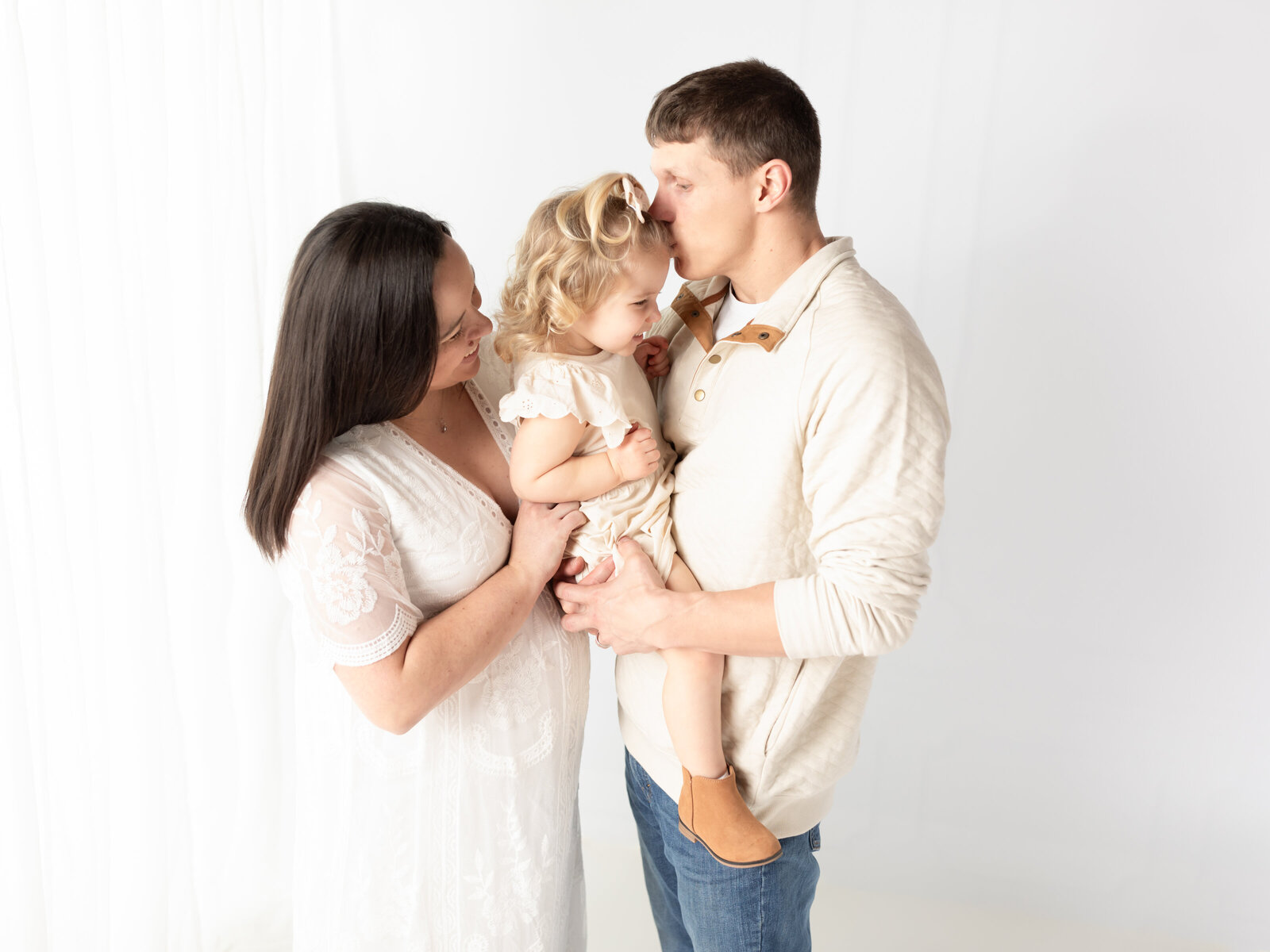 pregnant mother in white lace dress hugging daughter and husband for maternity photos