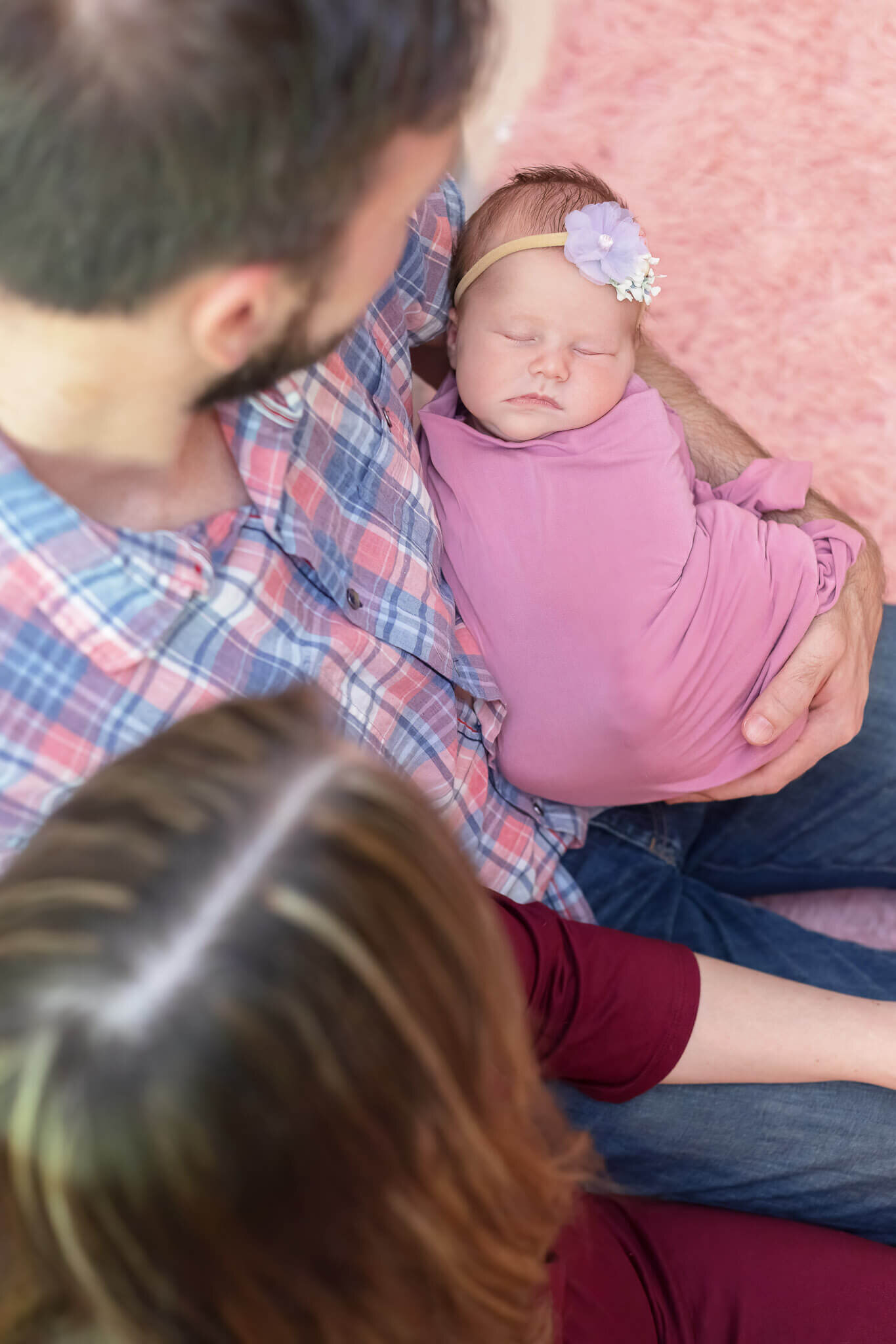 An above view looking down on parents holding their newborn girl wrapped in pink.