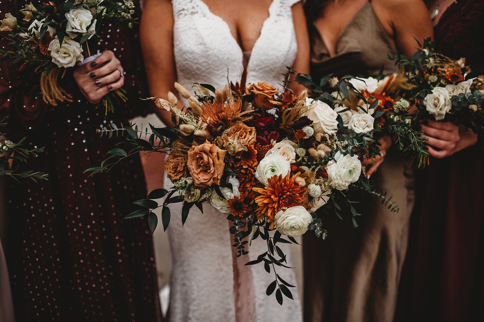 Baltimore photographers photographs bride holding a warm toned wedding bouquet while standing with her bridesmaids who are also holding bouquets while wearing their bridesmaids dresses