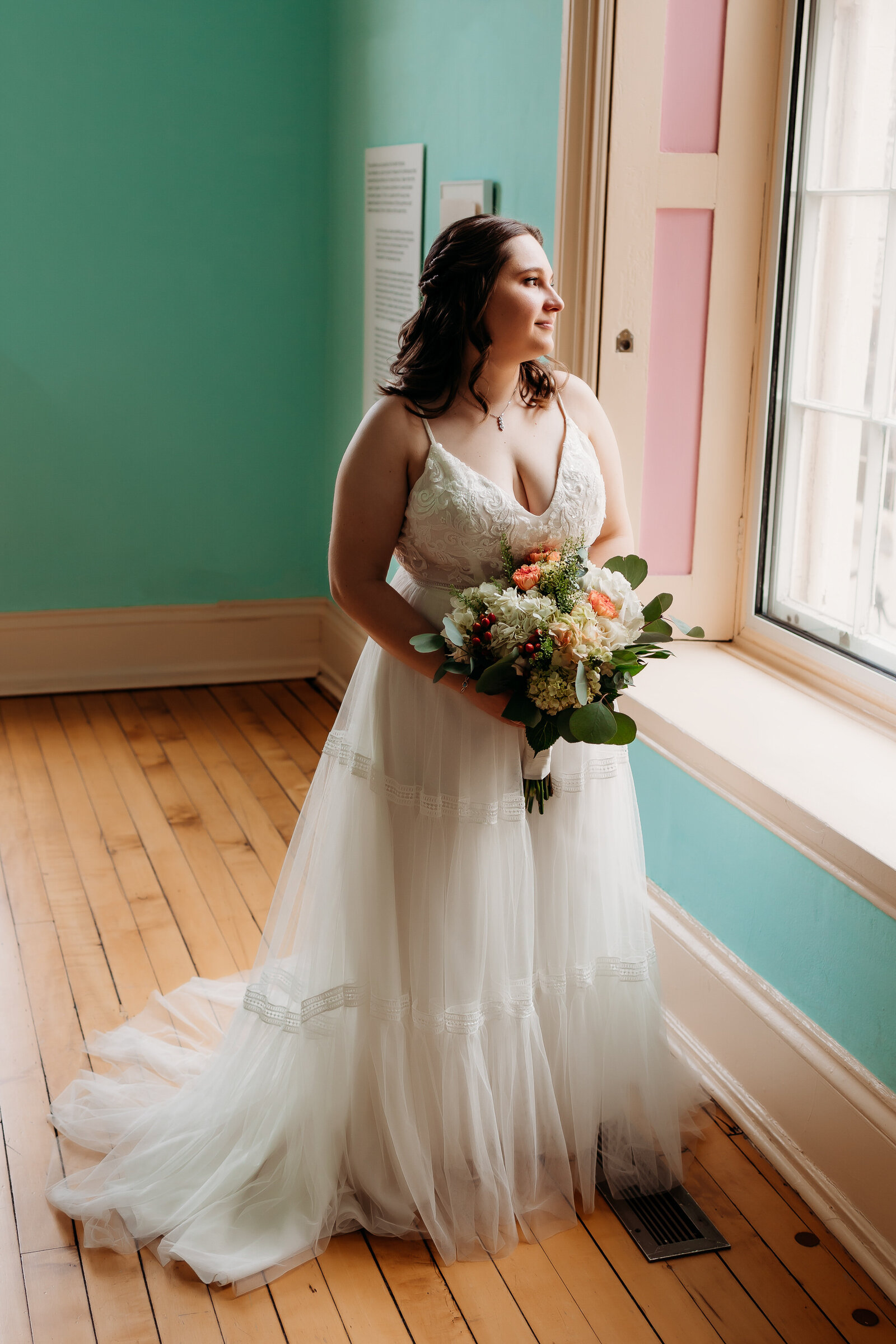 Bride stands with her bouquet gazing out the window for a photo