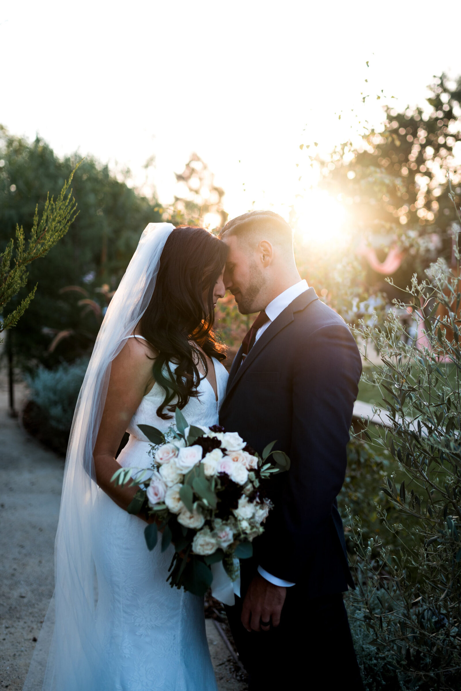 Wedding couple with faces touching, smiling with eyes closed, with the sun setting in the background, taken by Winnipeg Wedding Photographer, Kyle Cottrell.