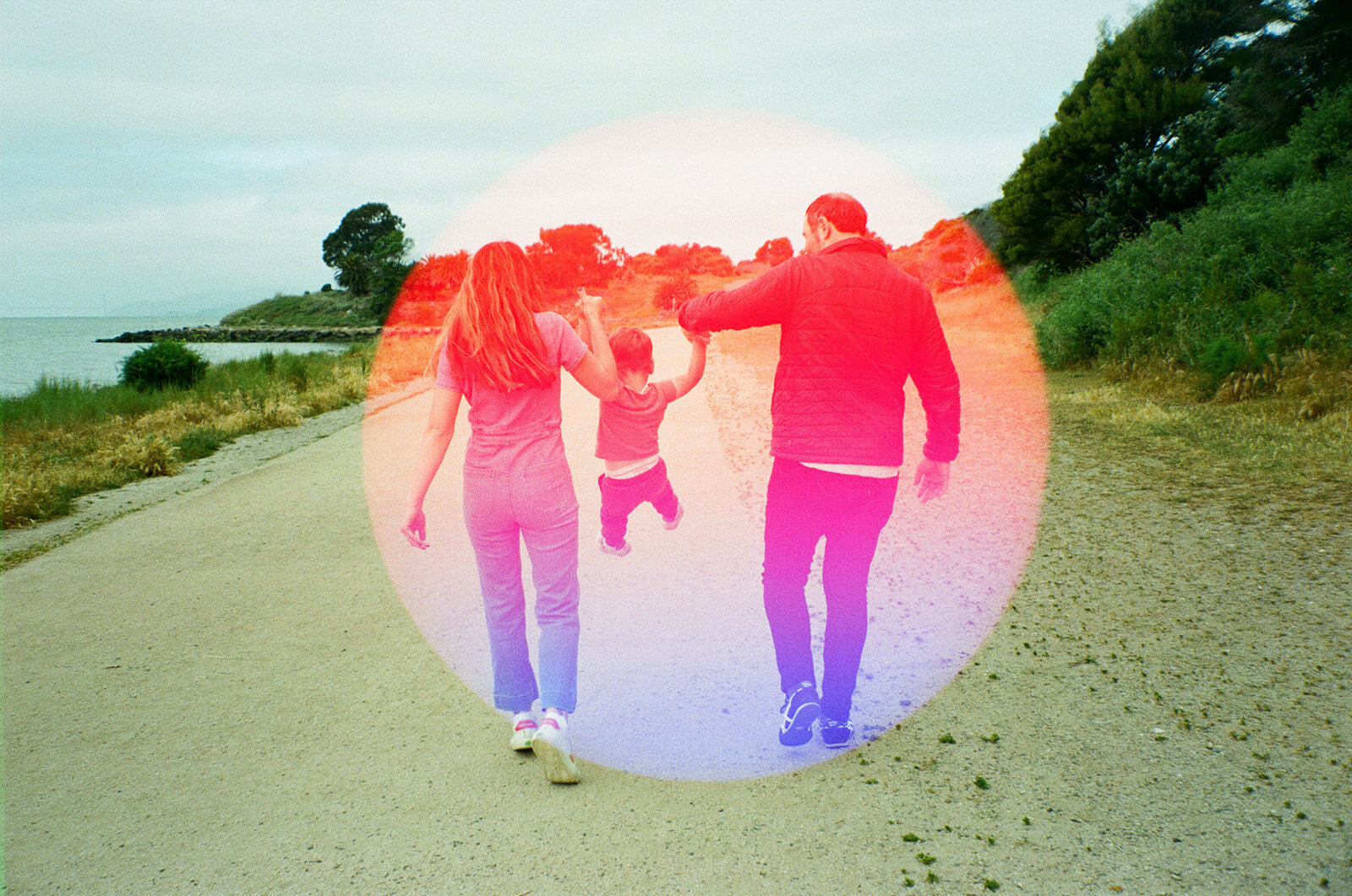 film photograph with a circular light leak of a mom and dad walking and swinging their toddler between them