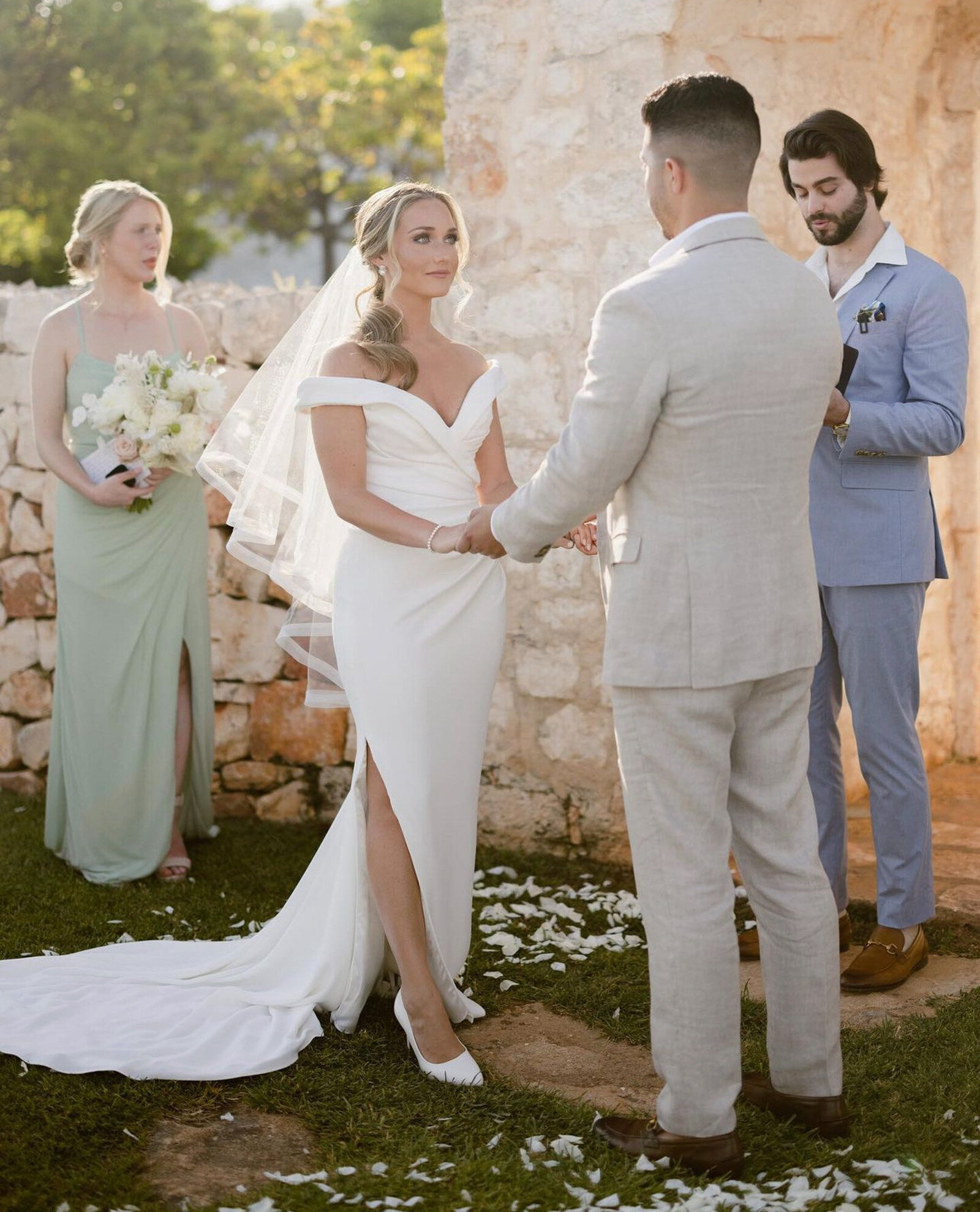 Bride and groom holding hands during their outdoor ceremony with the officiant and bridesmaid visible