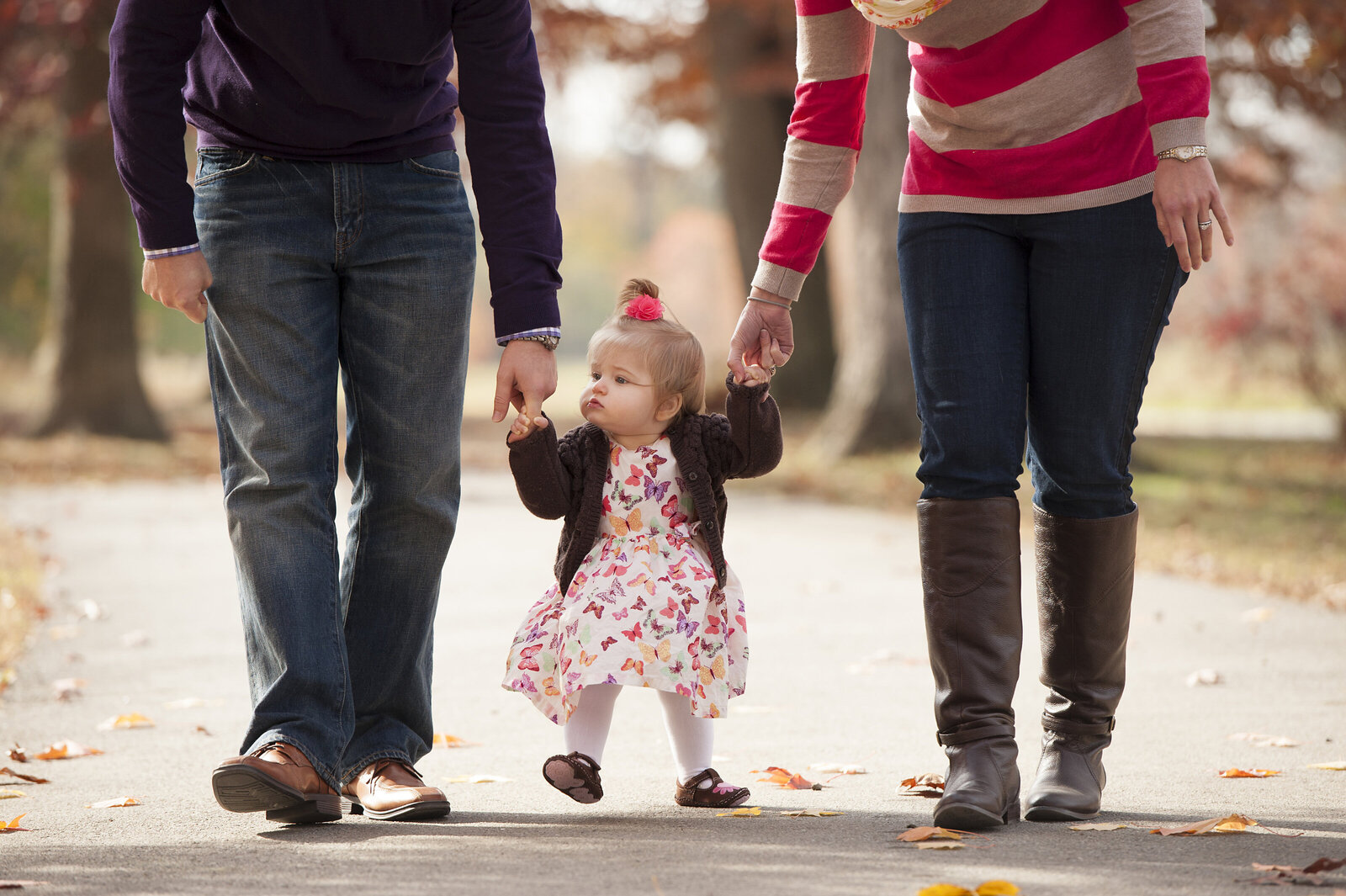 A toddler holding both their parent's hands as they walk together 