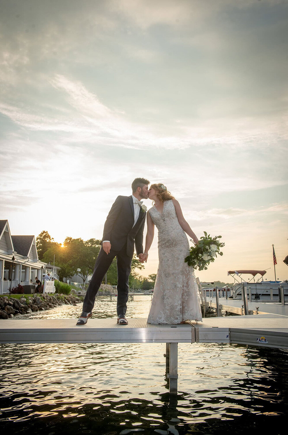 bride and groom kiss on lakeside dock at sunset