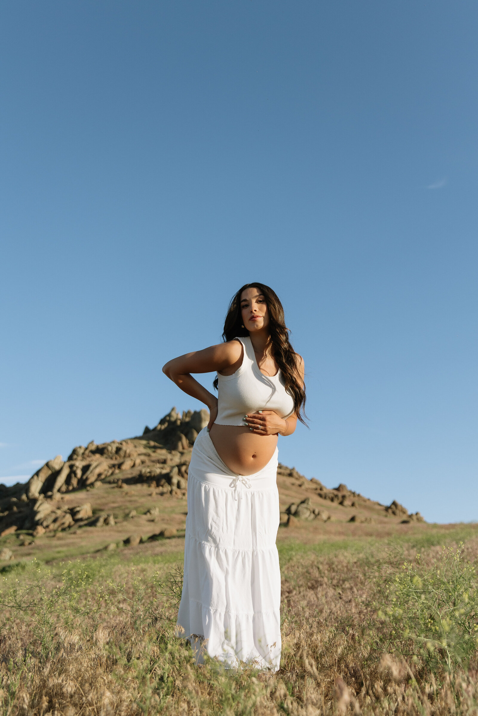 Peaceful photo of pregnant woman in open meadow under mountain sky