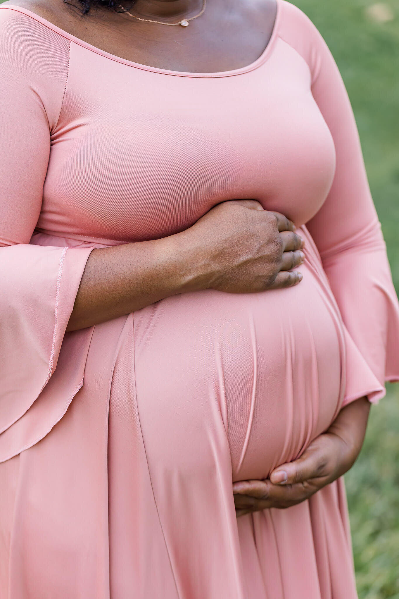 A side view of a pregnant woman's belly in a pink dress during her maternity session.