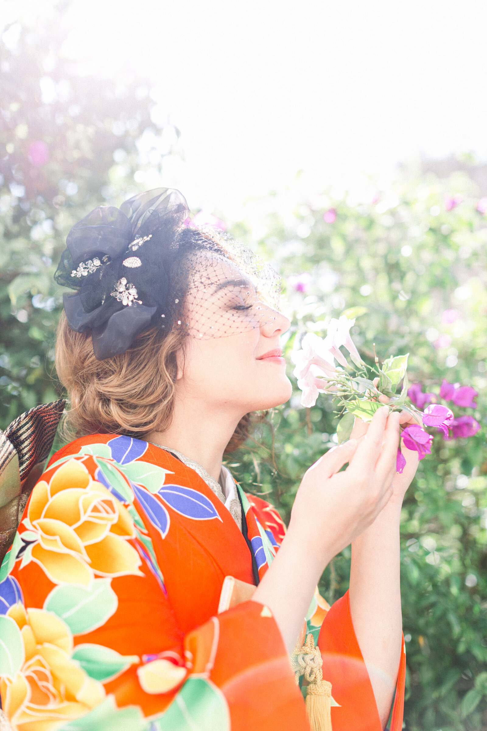 Bride in vibrant orange floral wedding kimono rental holding delicate flowers and smiling softly at All Saints Episcopal Church, Pasadena Los Angeles | オールセインツ教会 オレンジの花柄振袖 花嫁が花を手に微笑む 着物レンタルウェディング