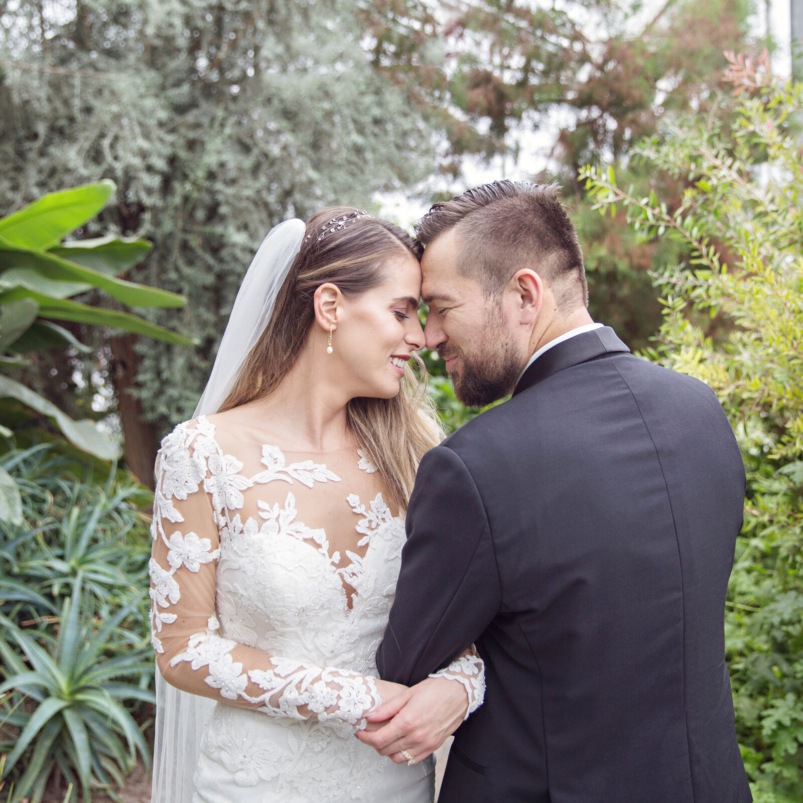 birde and groom foreheads together in greenhouse