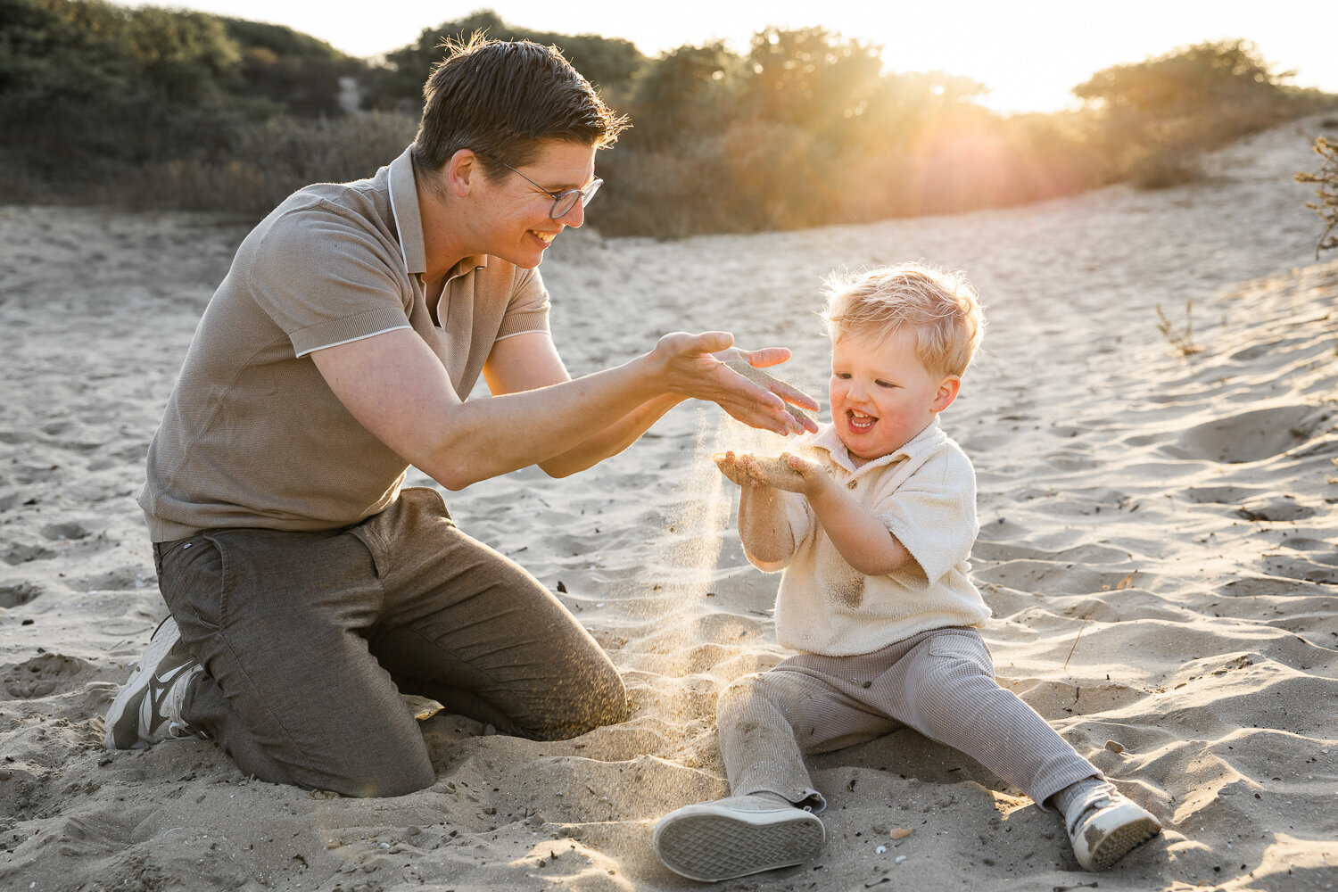 Vader en zoon spelen met het zand tijdens een golden hour gezinsshoot in de duinen.