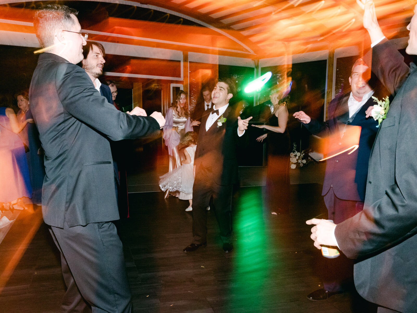 The guests hit the dance floor at a wedding with colorful lights in the background.