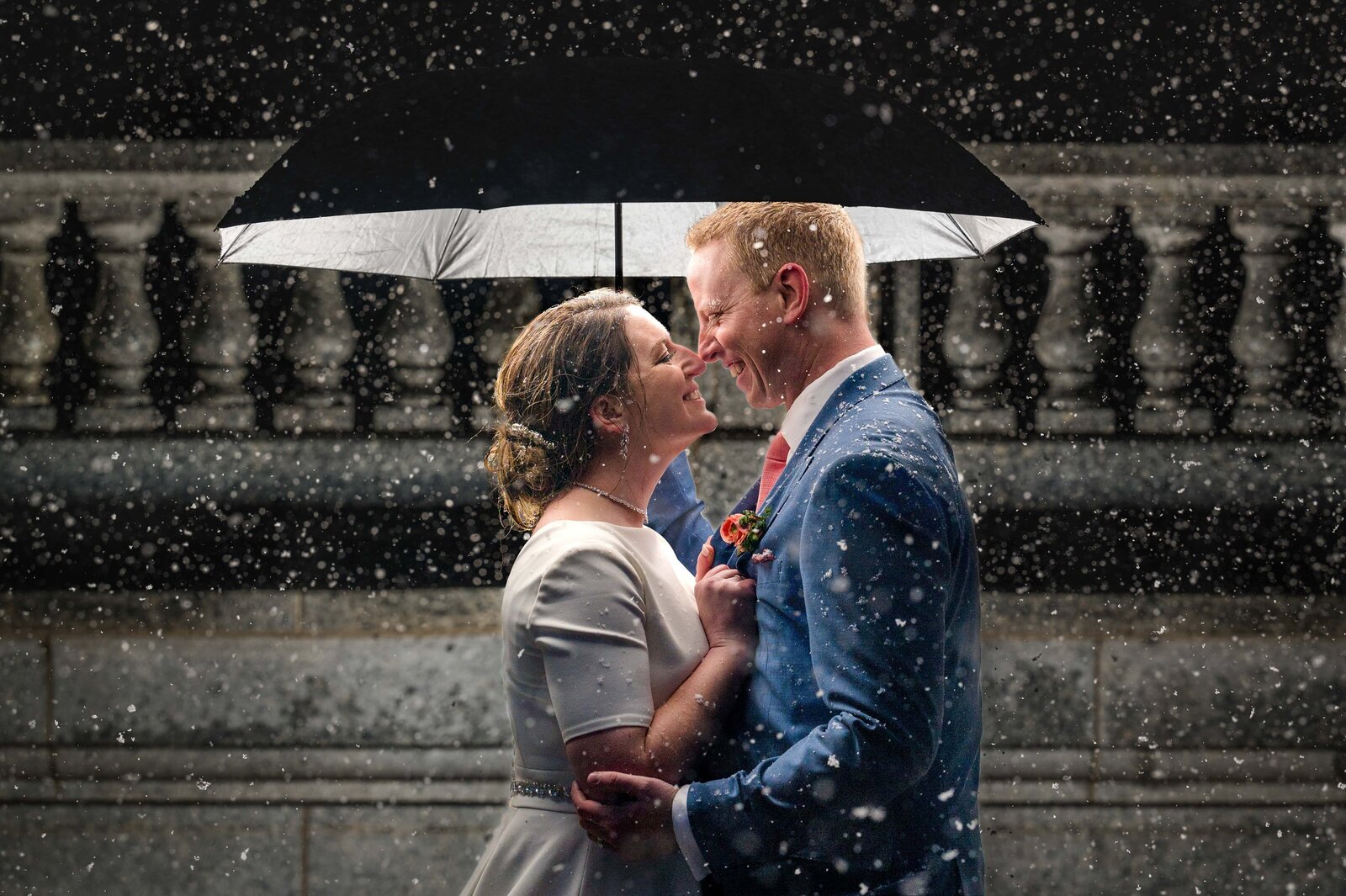 Bride and groom holding umbrella at the Utah State Capitol while it rains.
