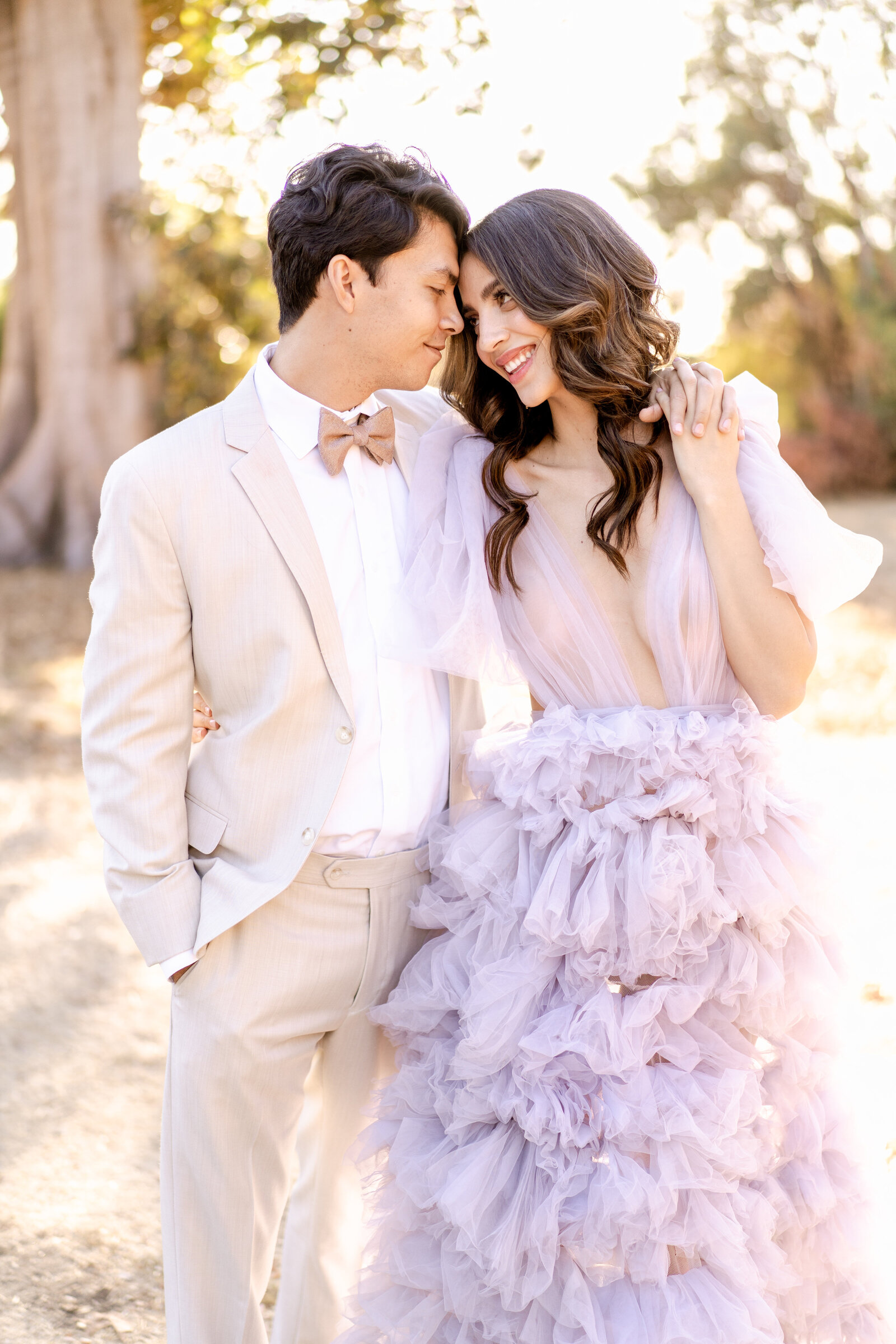 Portrait of bride and groom in a lavender gown and cream suit outdoors.