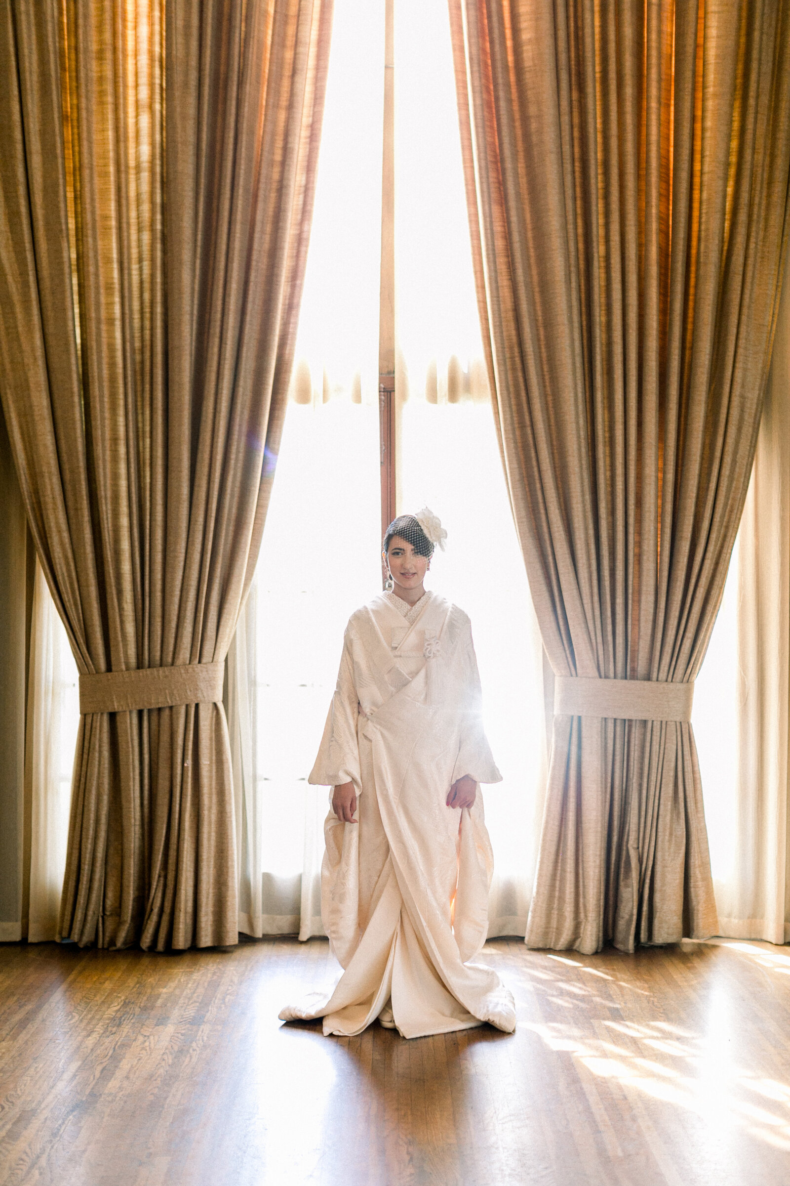 Full-length portrait of bride between grand curtains wearing white shiromuku at The Ebell Club Long Beach, Los Angeles California. Available for wedding kimono rental in Los Angeles | 大きなカーテンの中央に立つ白無垢花嫁の全身ポートレート。ロサンゼルスのエベルクラブにて。着物レンタル可能。