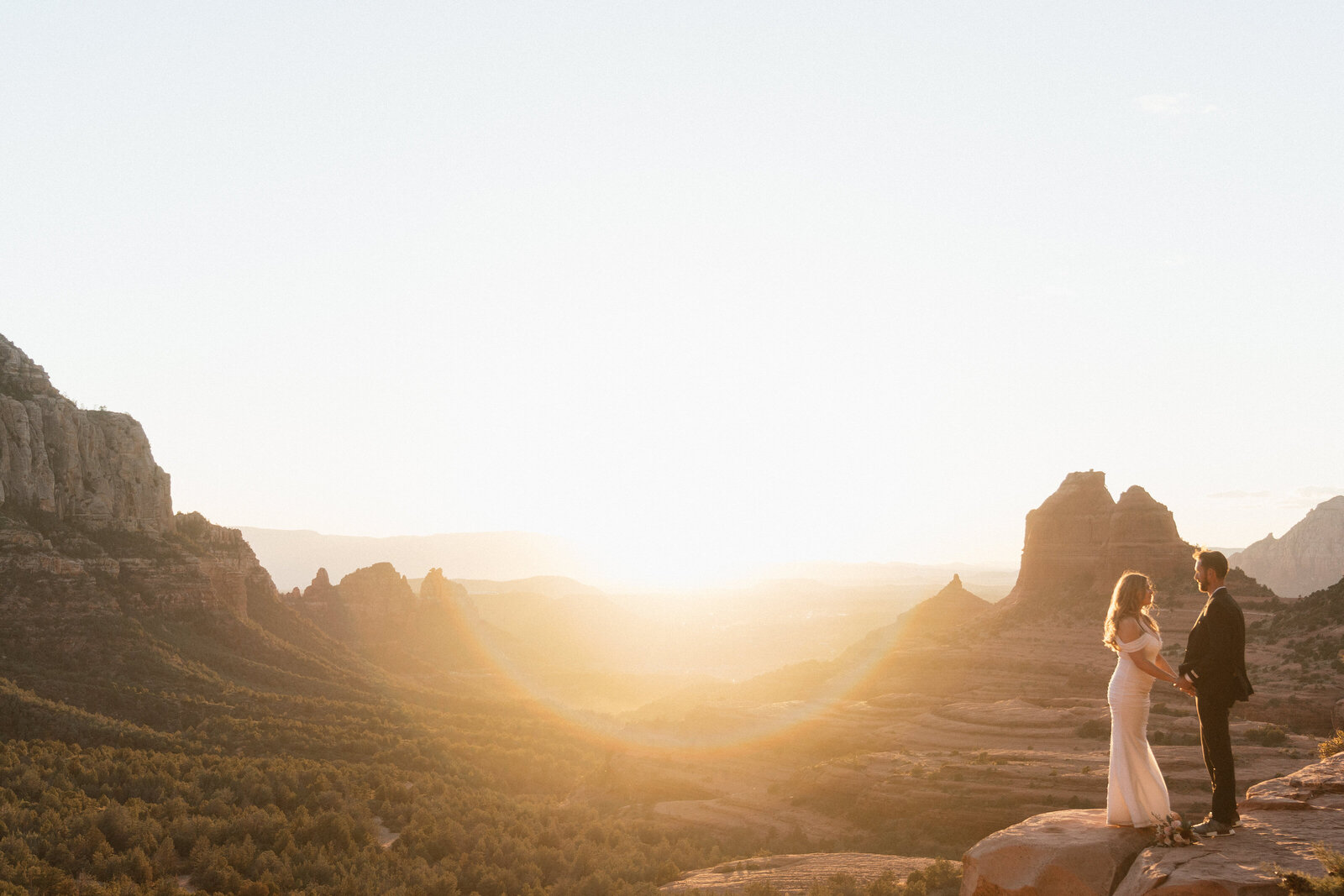 Bride and groom holding hands during a romantic sunset elopement at Merry Go Round Rock in Sedona, Arizona with red rock formations and golden light in the background.