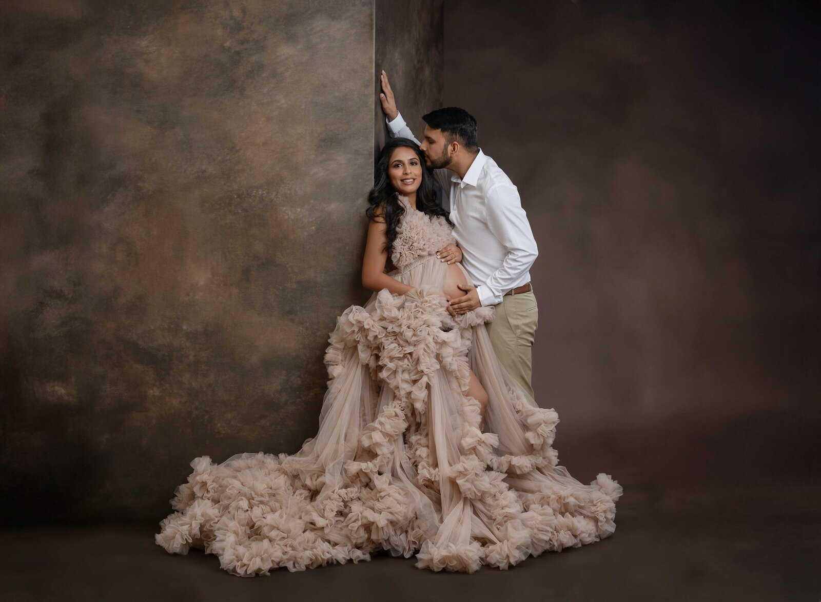 Pregnant women holding baby bump as Dad kisses her head. 