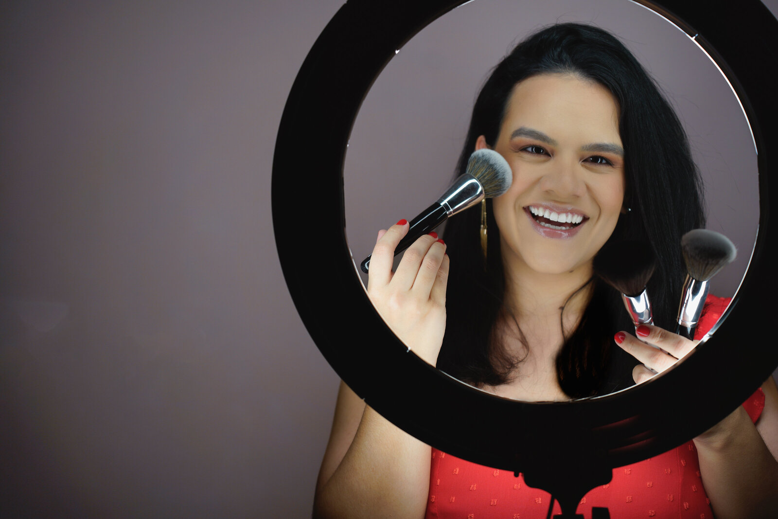 make up artist posing behind a ring light with brushes