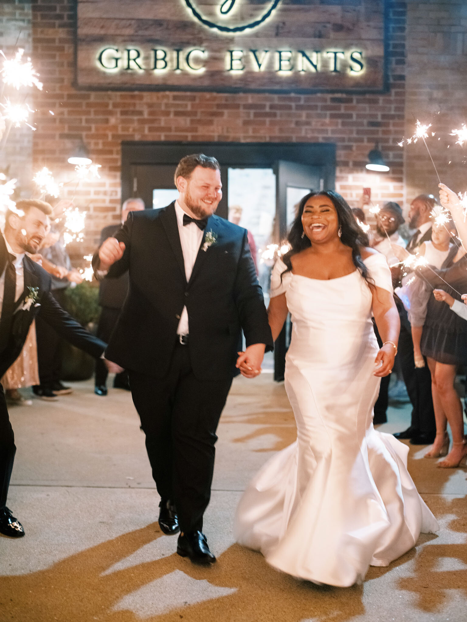 newlywed couples walking hand in hand while guests holding sparklers during their wedding send-off, smiling and celebrating.
