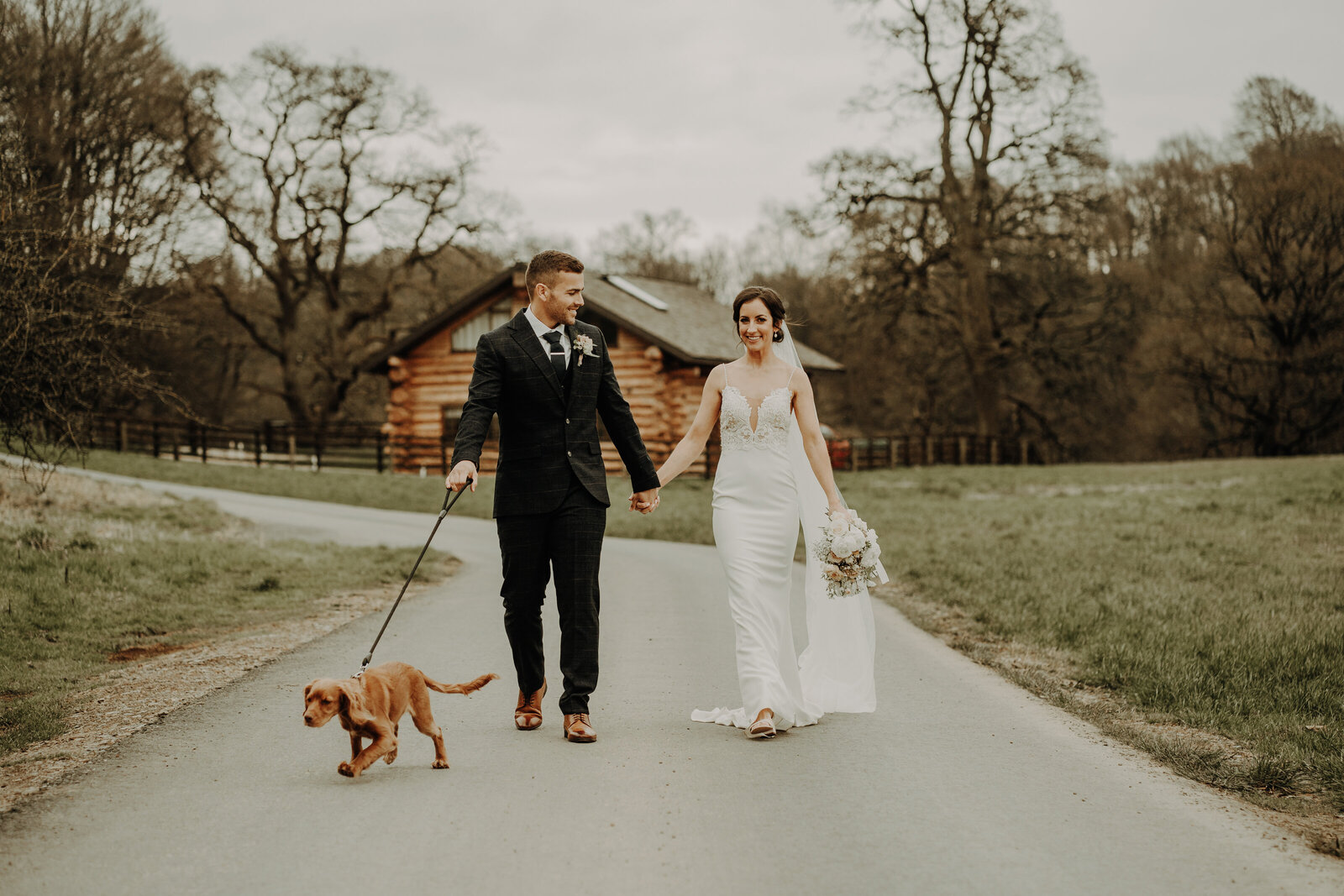 bride and groom walking hand in hand and walking with dog toward camera with log cabin in background fun aberdeen wedding photography